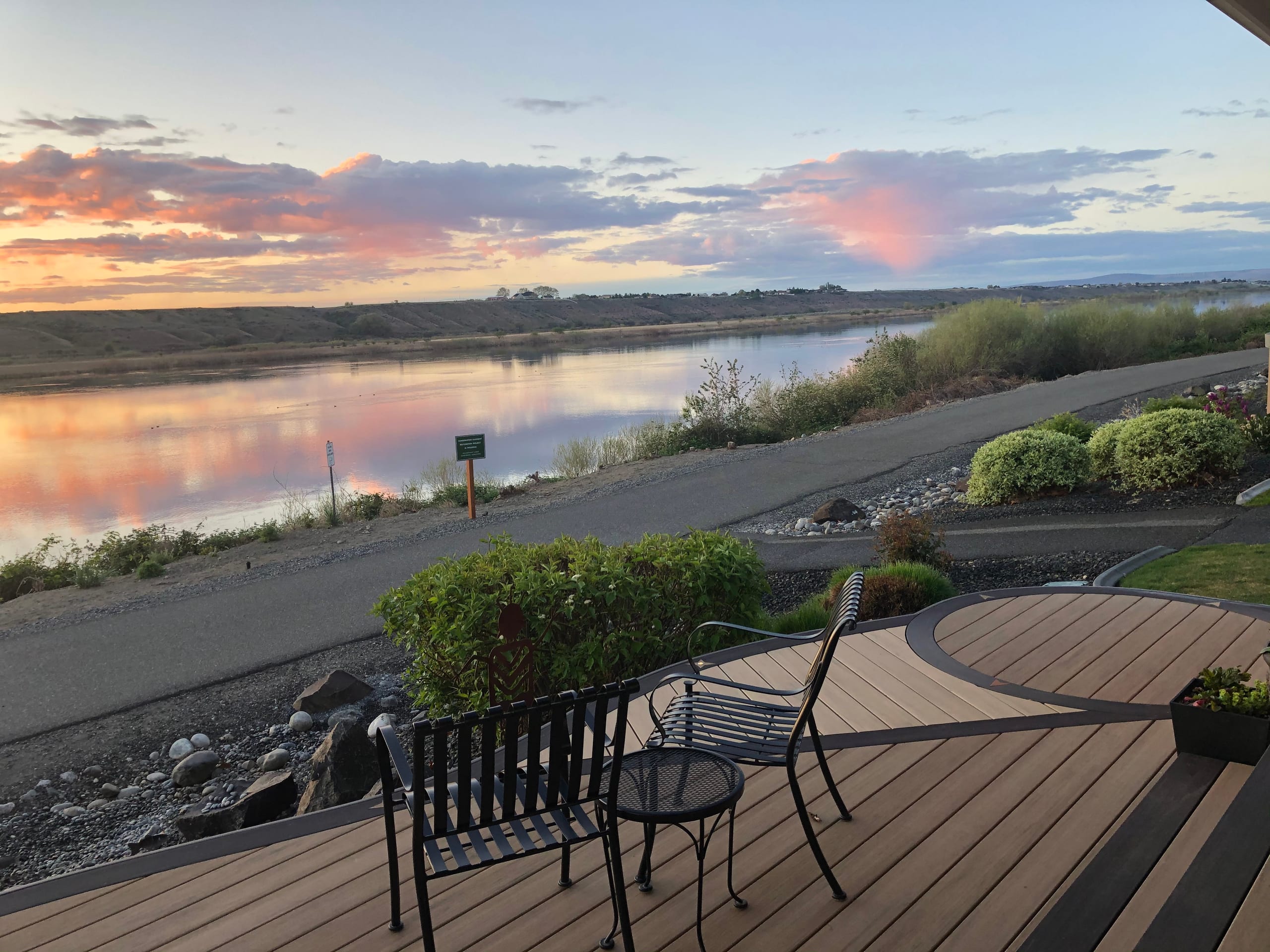 Deck with a curved inlay and black metal bistro chairs overlooking a river at sunset