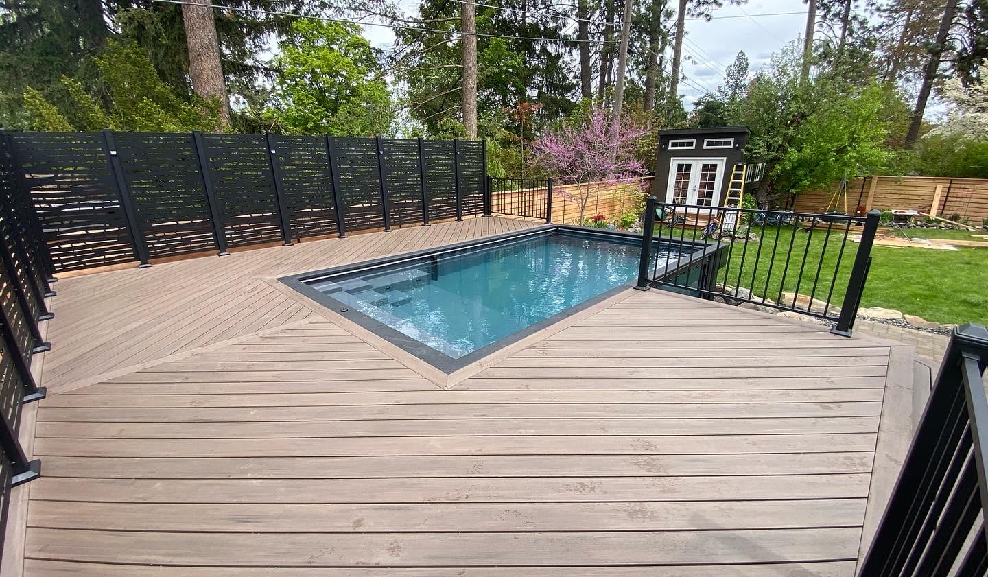 Diagonal-pattern deck around an inset rectangular pool with black railing and privacy screens