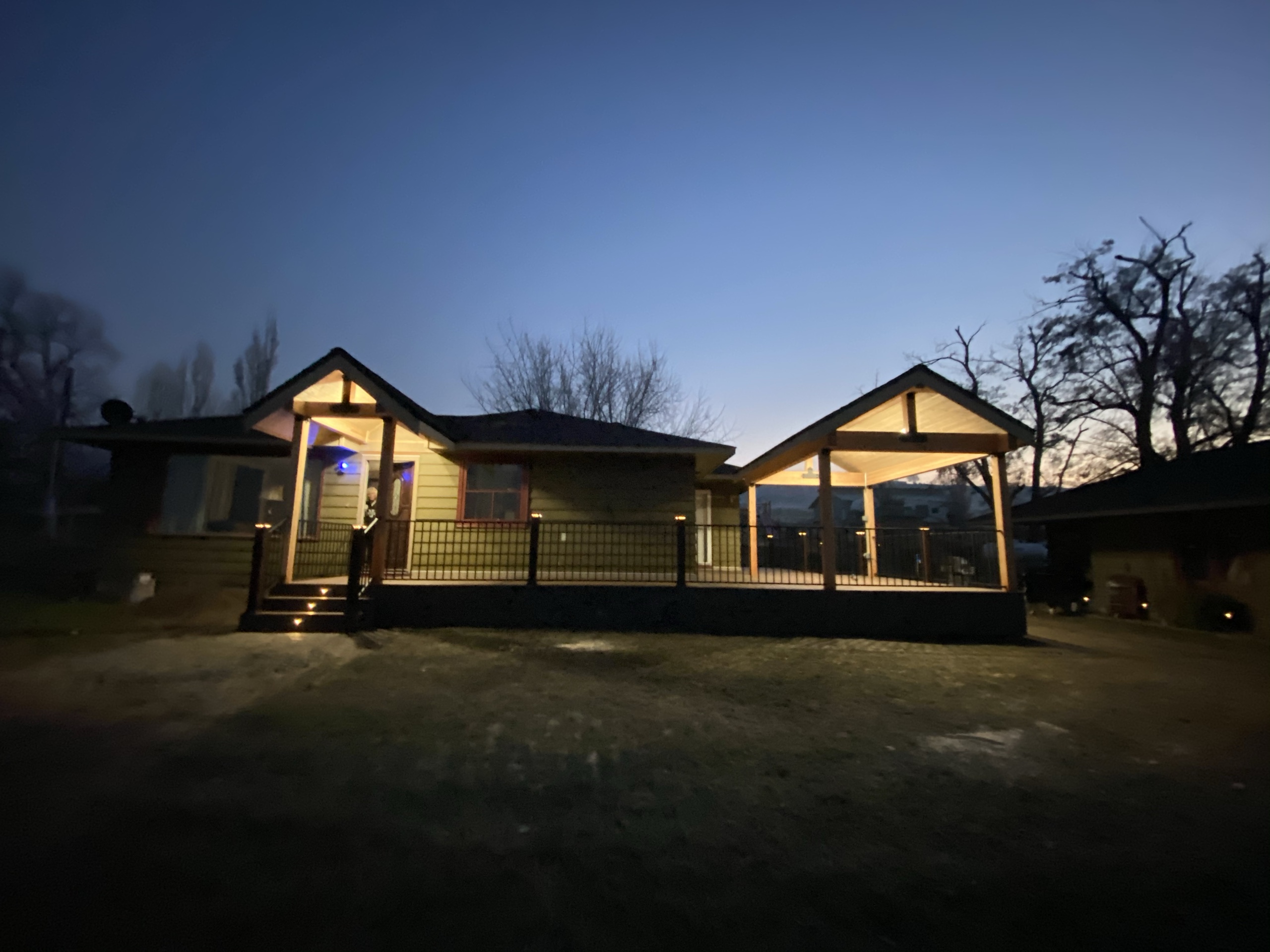 Dusk view of house with new lit entry porch and gabled covered deck, glowing ceilings, railing and steps