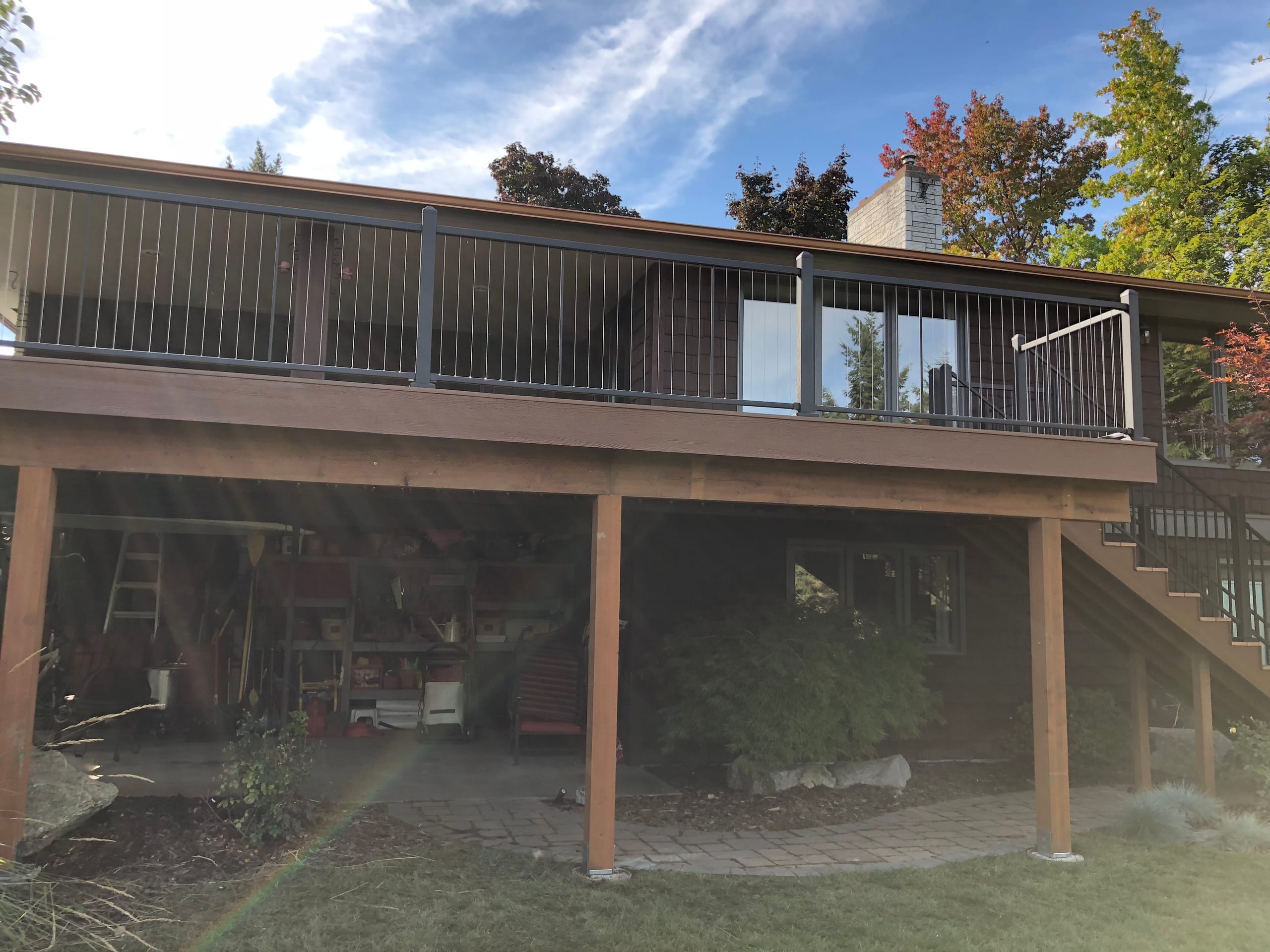 Elevated brown deck with black railing on stained posts over a cluttered storage space underneath, brown house
