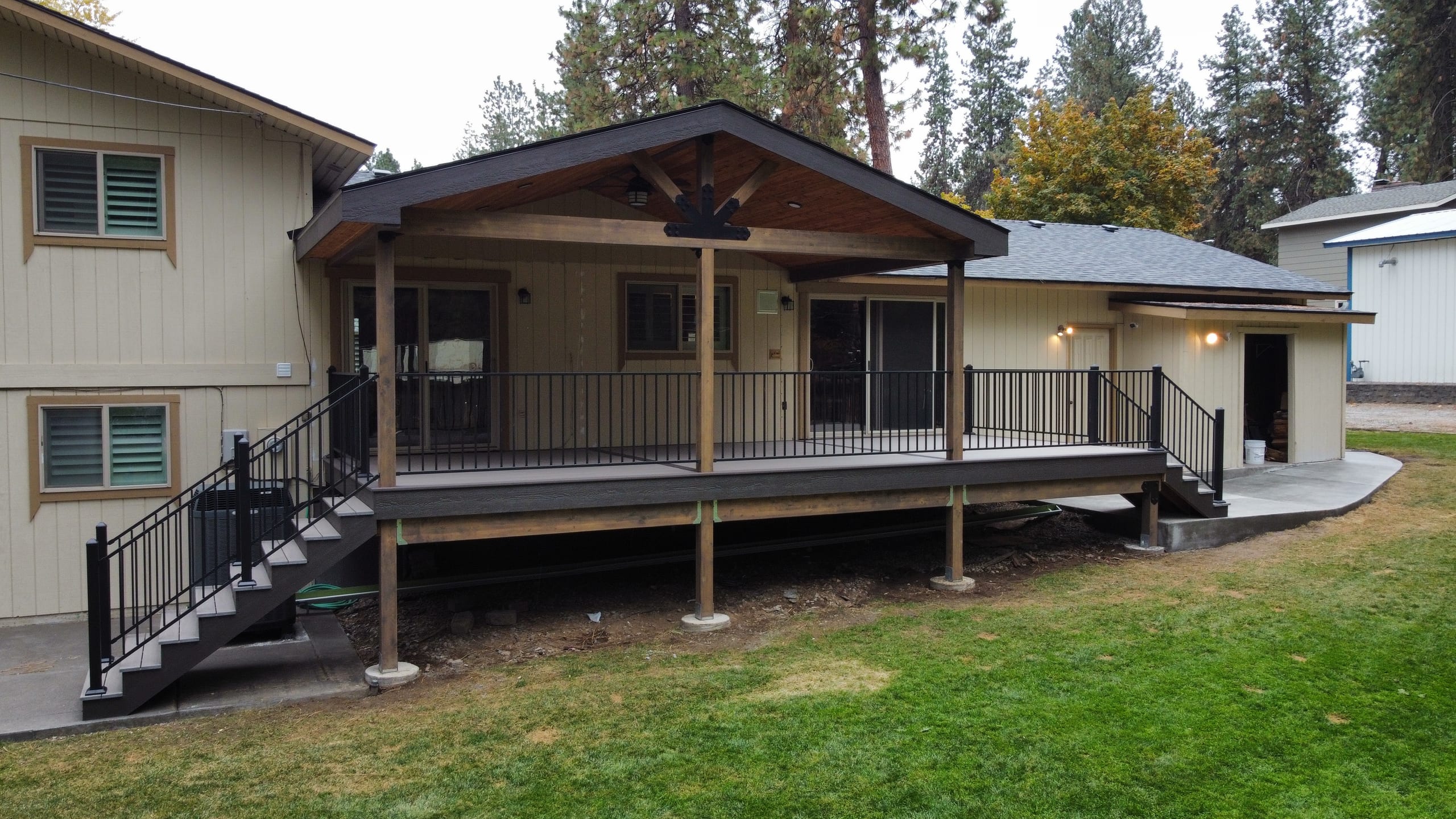 Elevated composite deck with gable cover, black picket railing and stairs, beige house and lawn