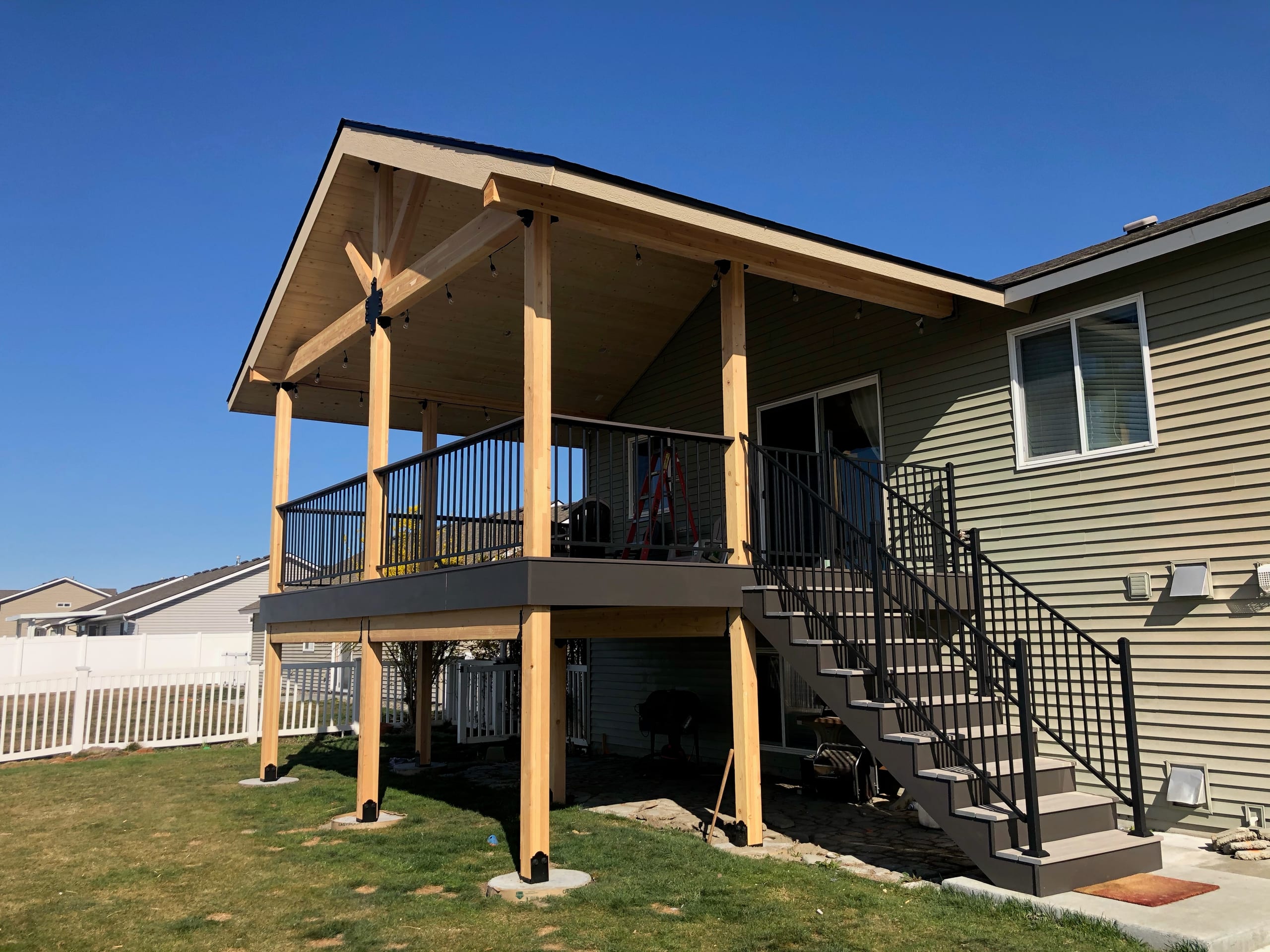 Elevated composite deck with gable cover, yellow posts, black picket railing and stair run, olive siding, blue sky