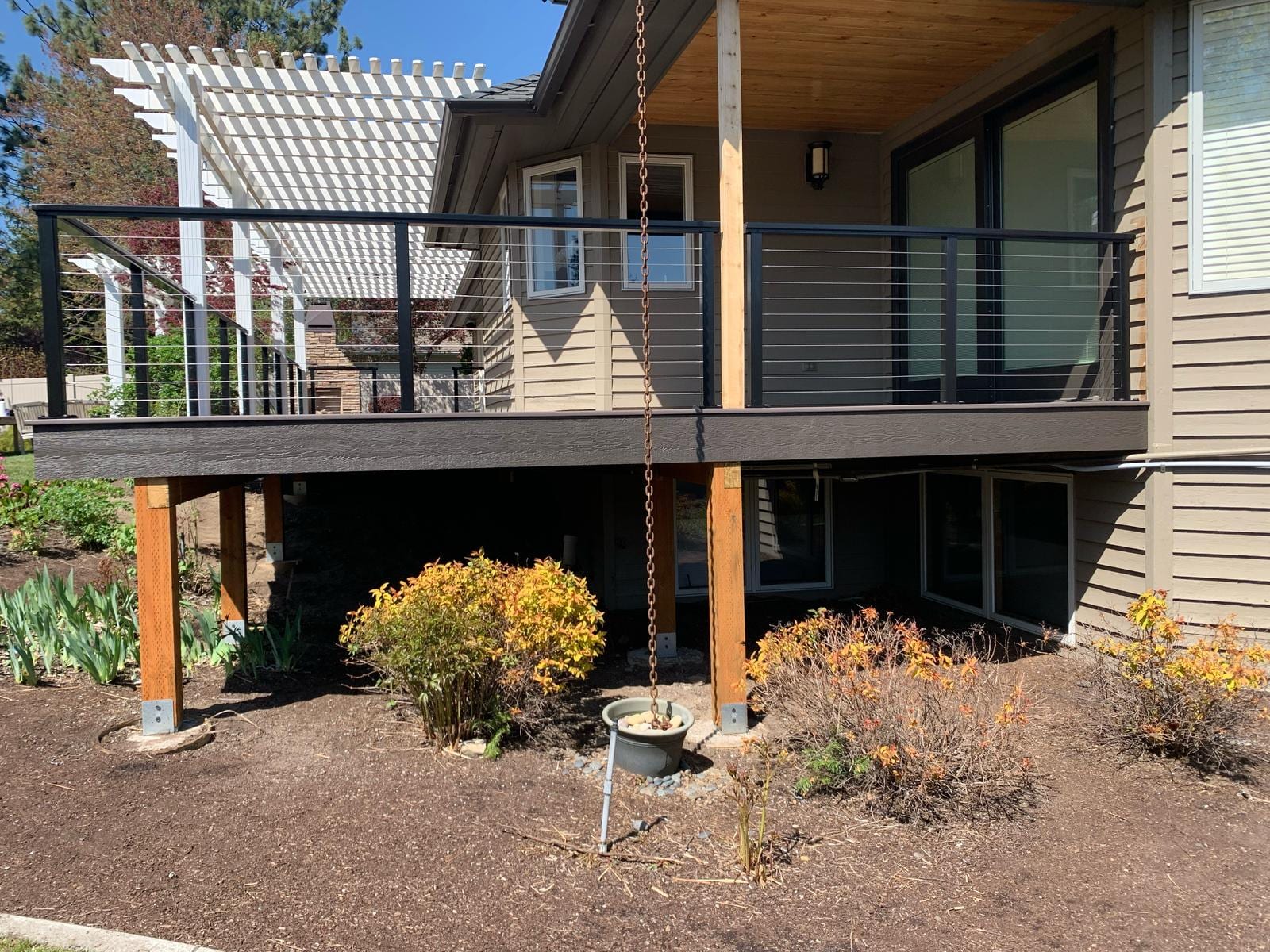Elevated deck with black cable railing and white pergola, cedar posts and landscaped beds below