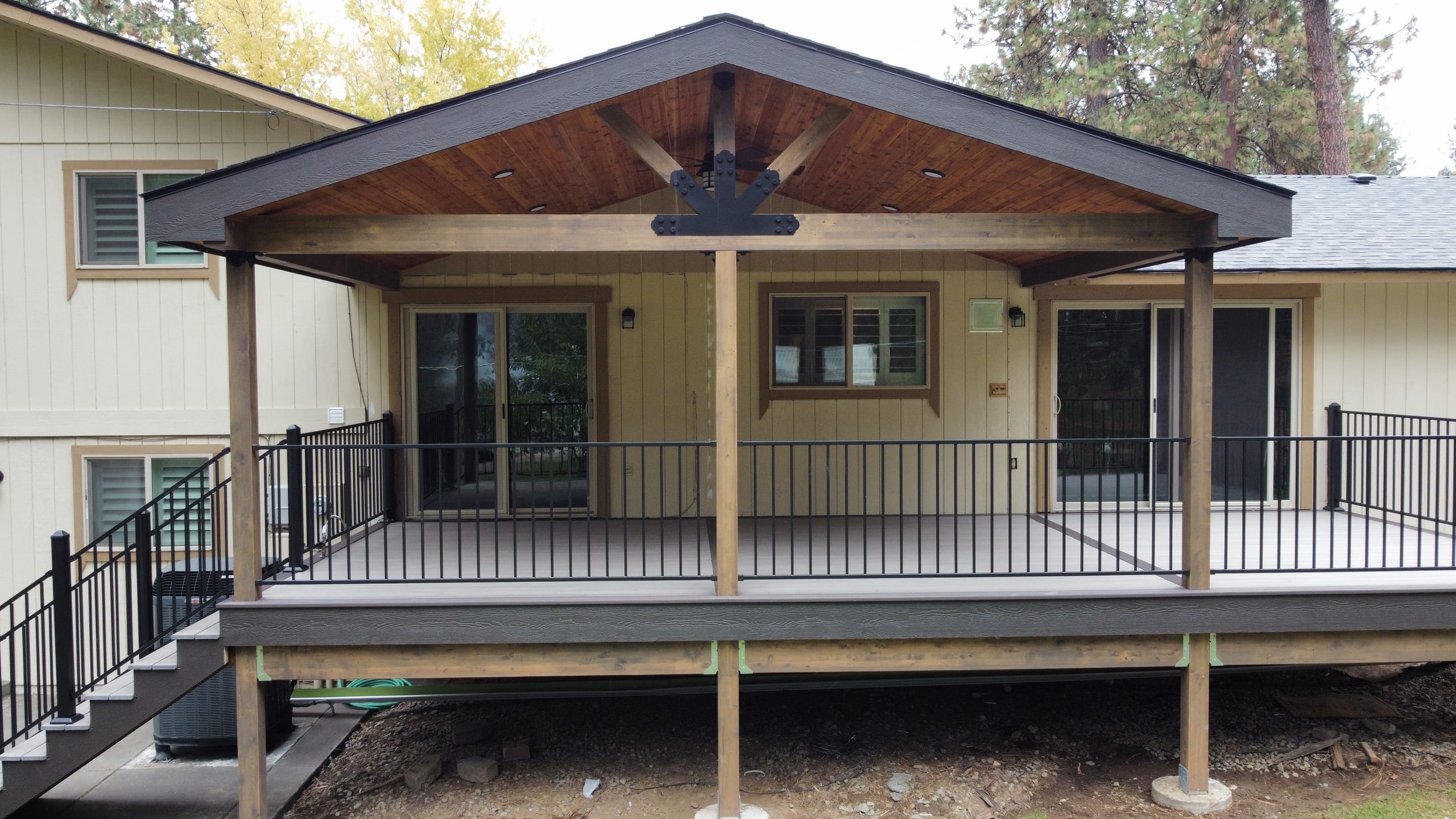 Elevated gray composite deck with black metal picket railing and stairs under a gable-roof cover with stained wood ceiling