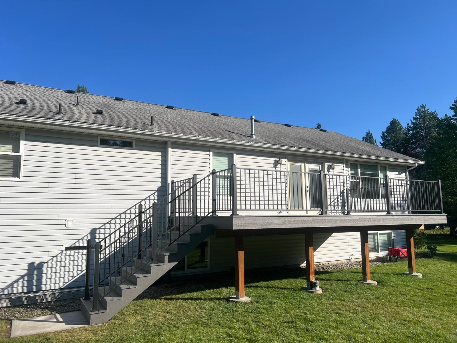 Elevated gray composite deck on posts with black metal railing and side staircase at the back of a white vinyl-sided home