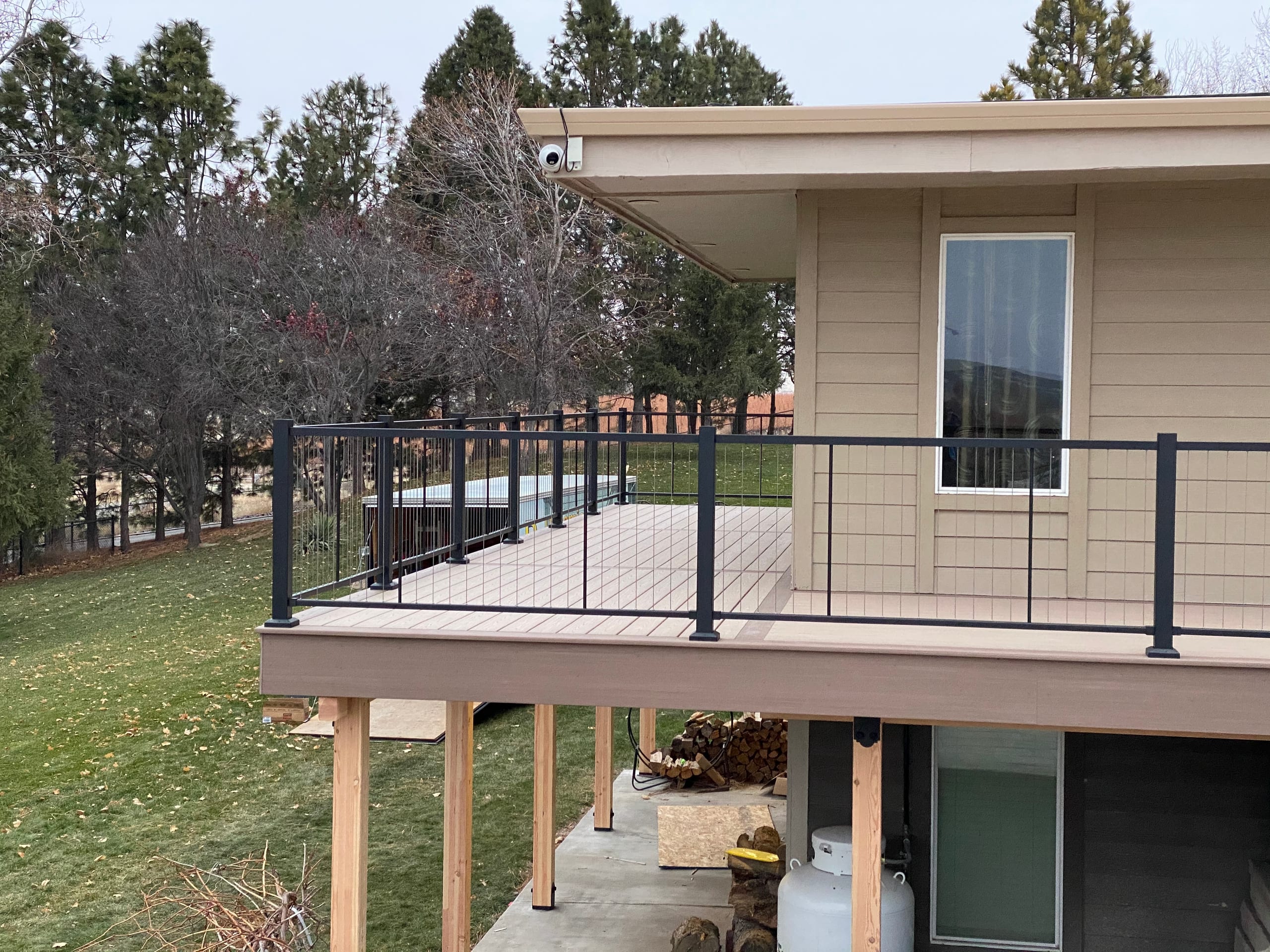 Elevated tan composite deck with black cable railing on a tan house, cedar posts, lawn below