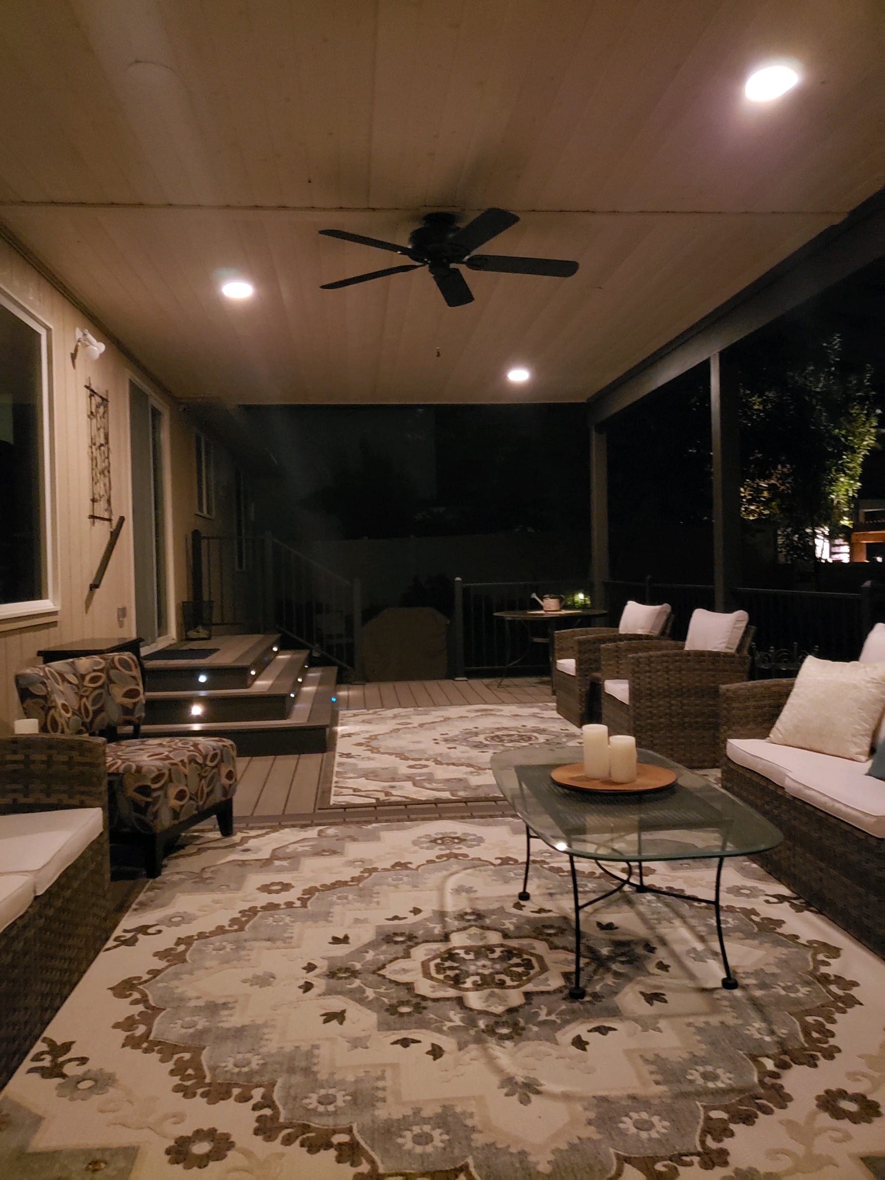 Evening enclosed porch with ceiling fan, recessed lighting, wicker furniture and rug, lit steps