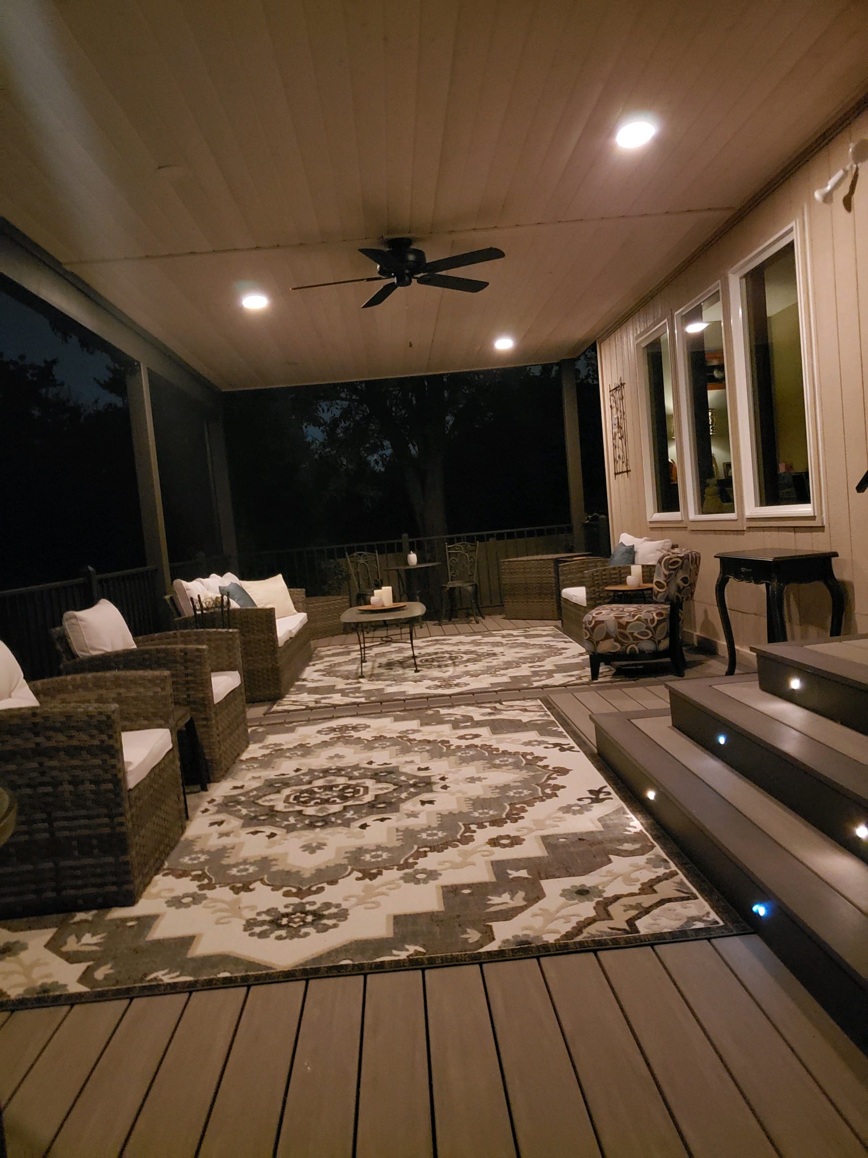 Evening screened porch with ceiling fan and recessed lights, wicker seating, patterned rug and lit composite steps