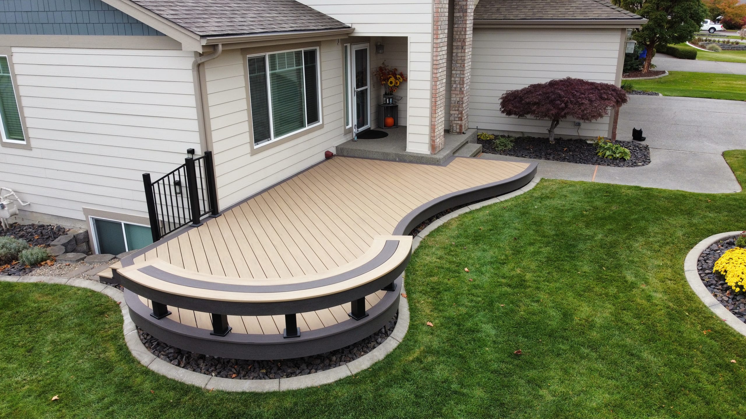 Front-entry curved beige composite deck with gray border and curved bench with black balusters, green lawn