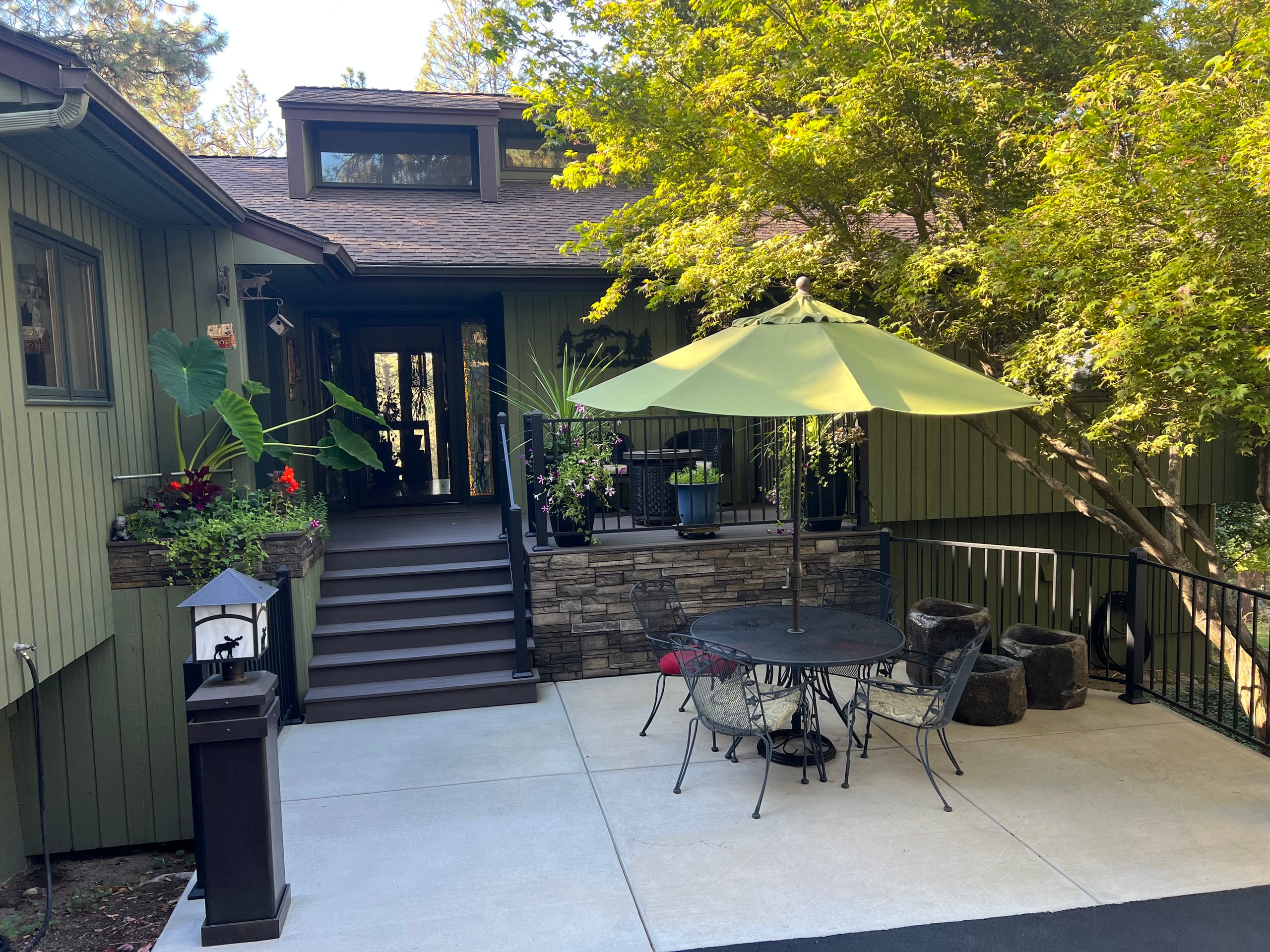 Front entry stairs and landing with black railing above a stone wall and concrete patio
