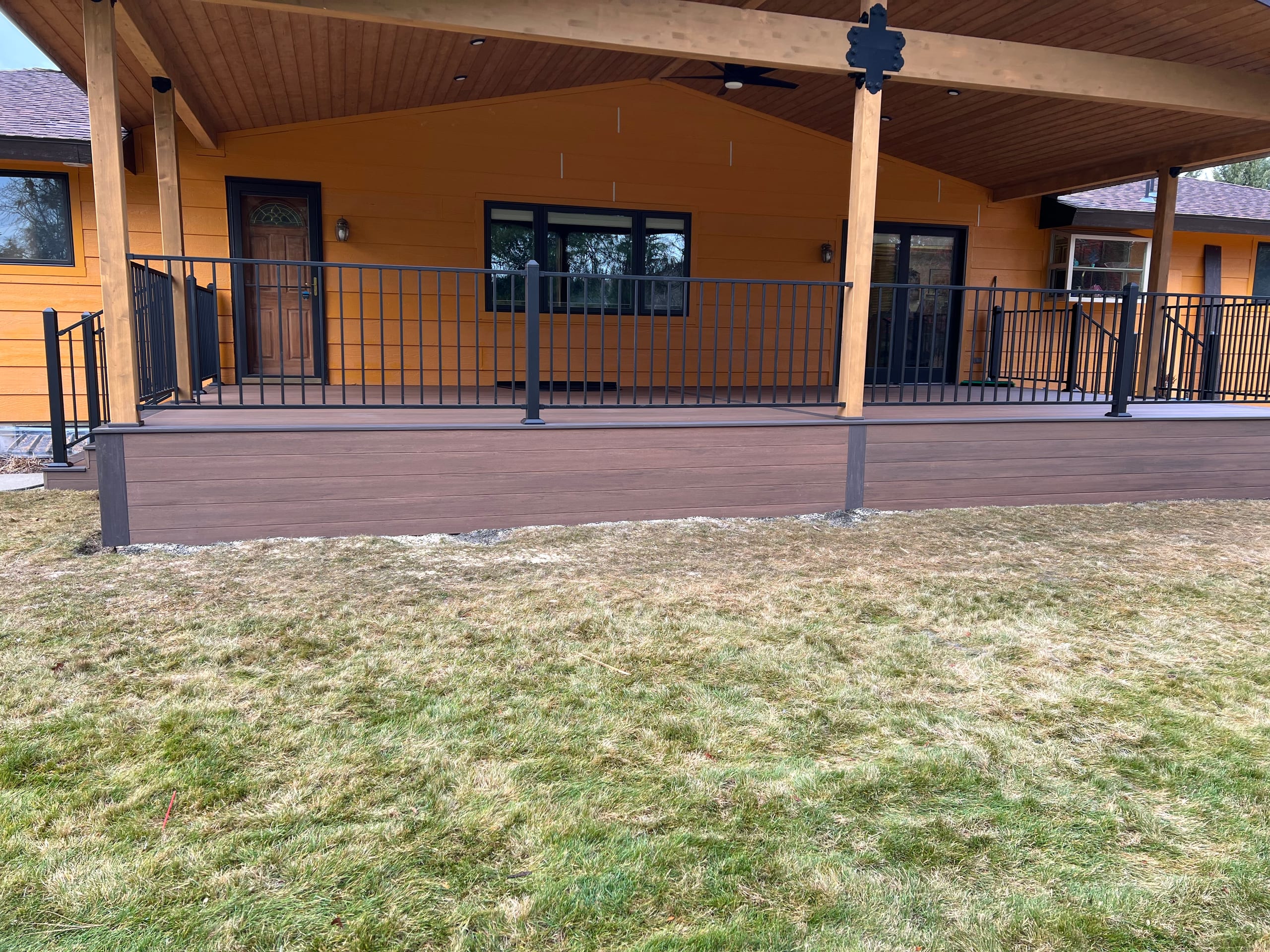 Front view of long covered deck on orange house with cedar posts