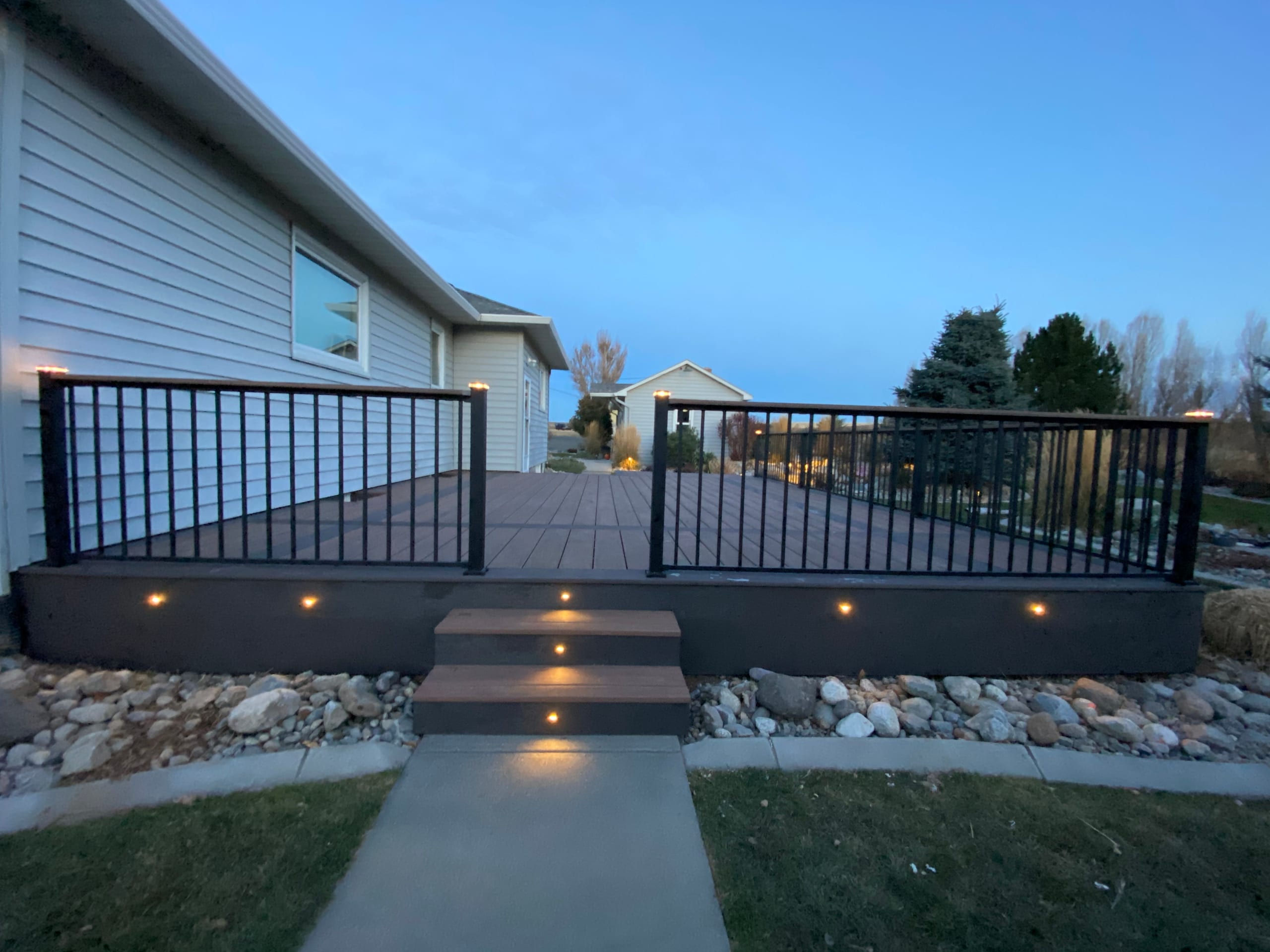 Front of low deck with centered lit steps, post-cap lights and fascia lights at twilight