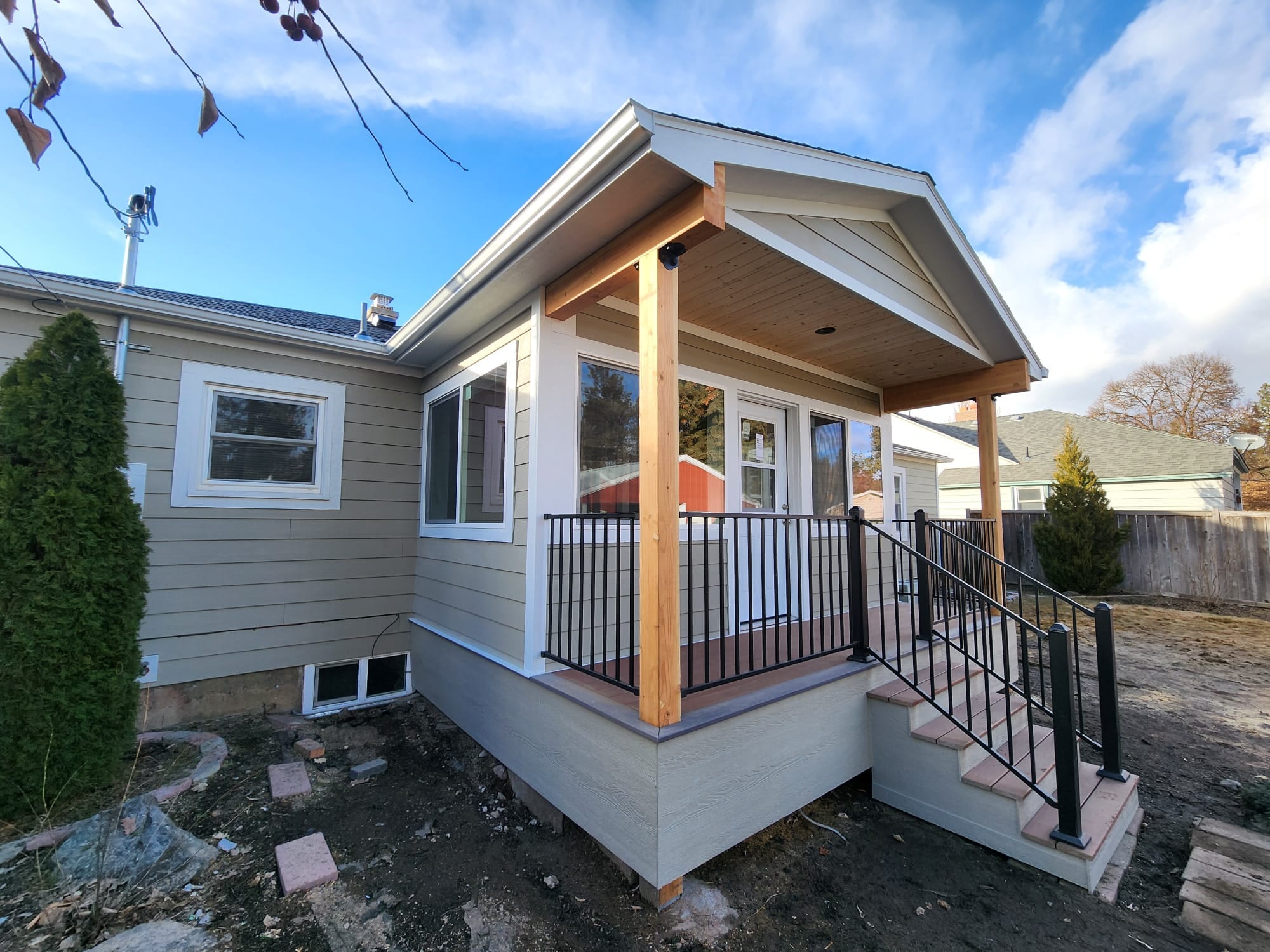 Gable-roof porch and enclosed room on a gray house with black picket railing and steps, blue sky