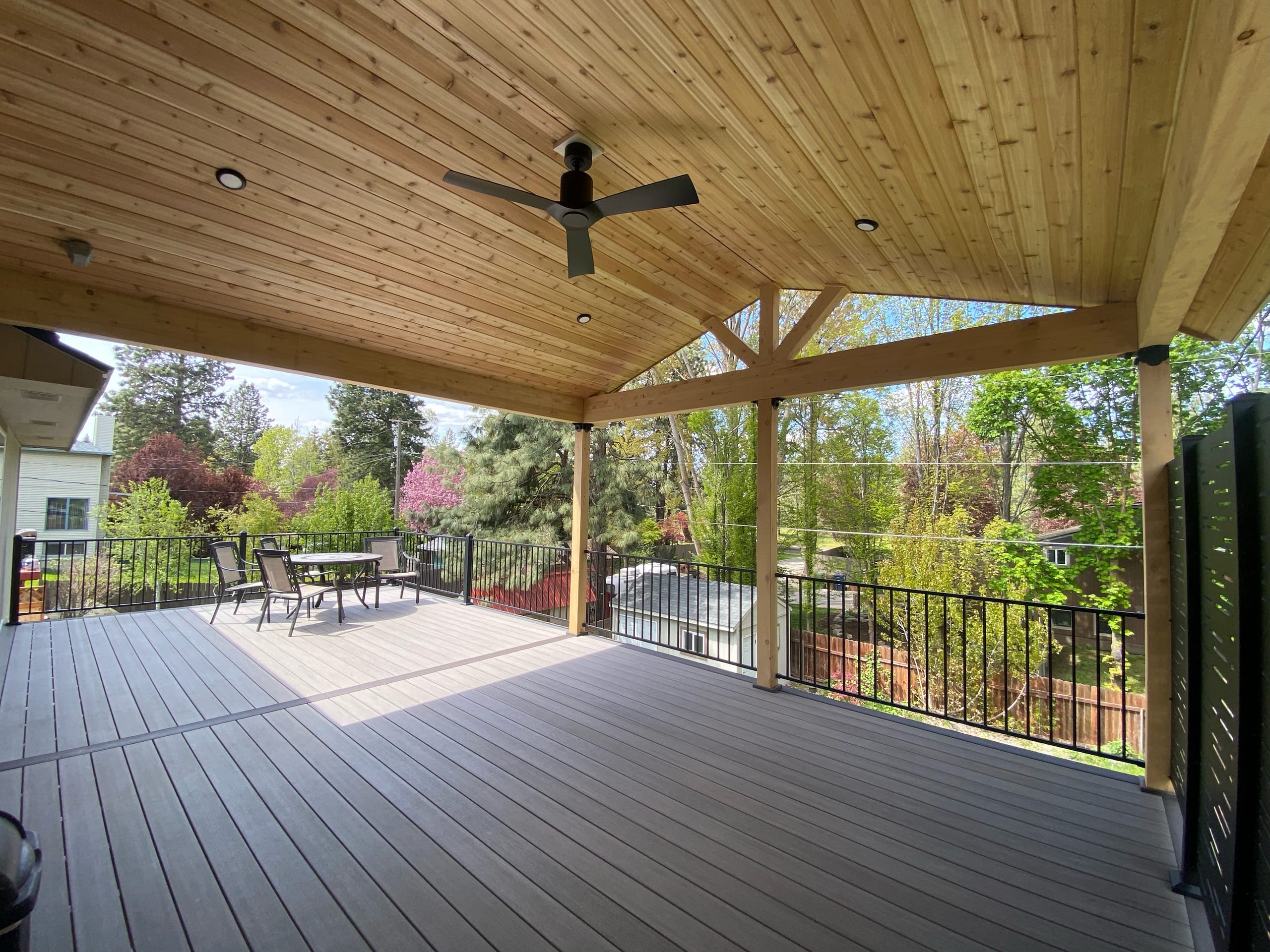 Gabled covered deck with cedar ceiling, fan, grey composite, black picket railing and patio set