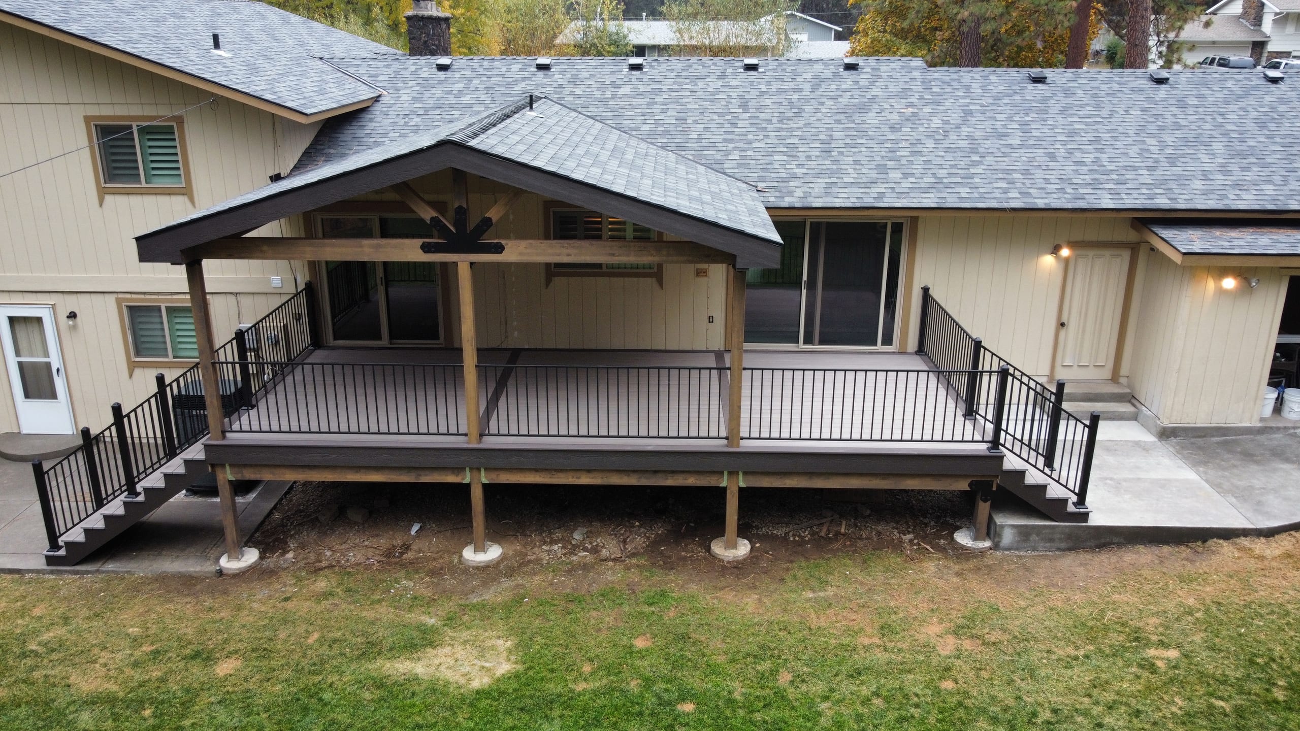 Gabled covered deck with ceiling fan and black railing on tan house