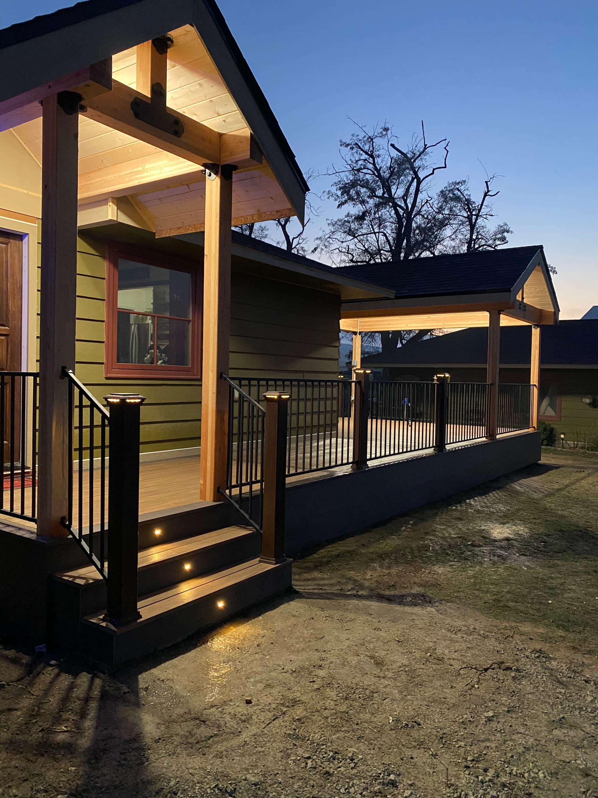 Gabled covered entry porch and covered deck at dusk with lit ceilings and steps, black picket railing