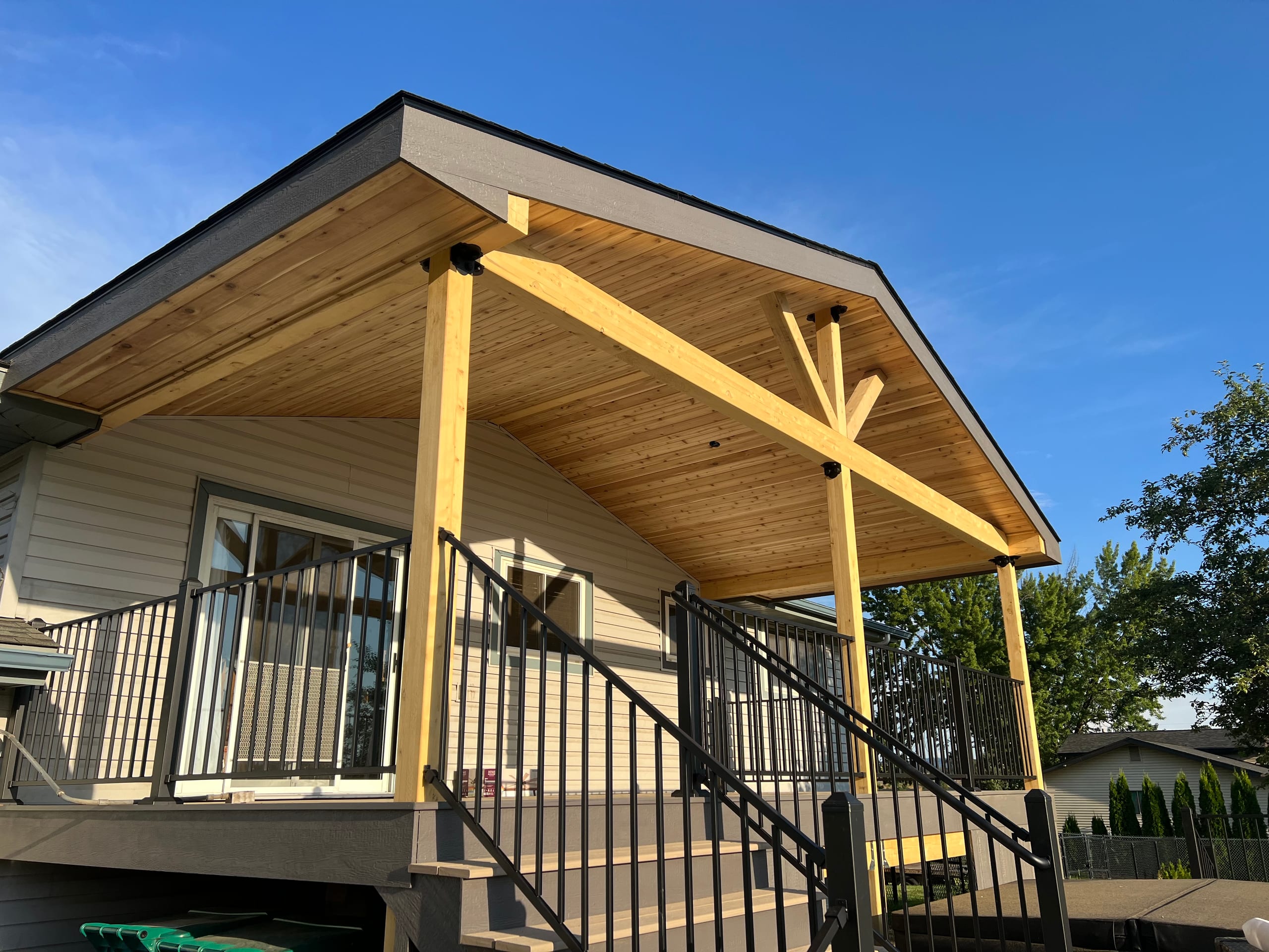 Gabled deck cover with natural wood beams, tongue-and-groove ceiling and black railing stairs
