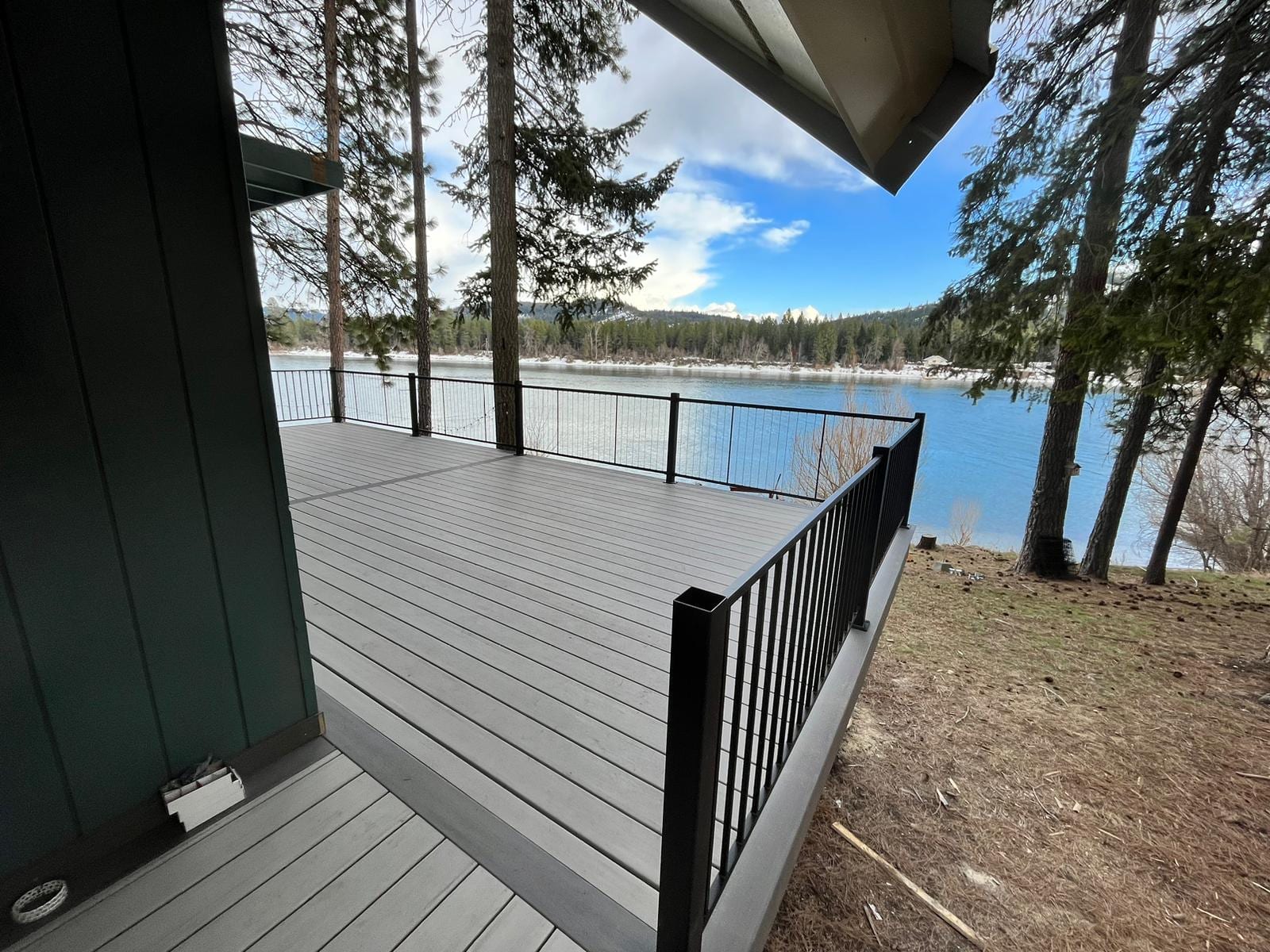 Gray composite deck with black metal railing overlooking a lake through pine trees, wide-angle view