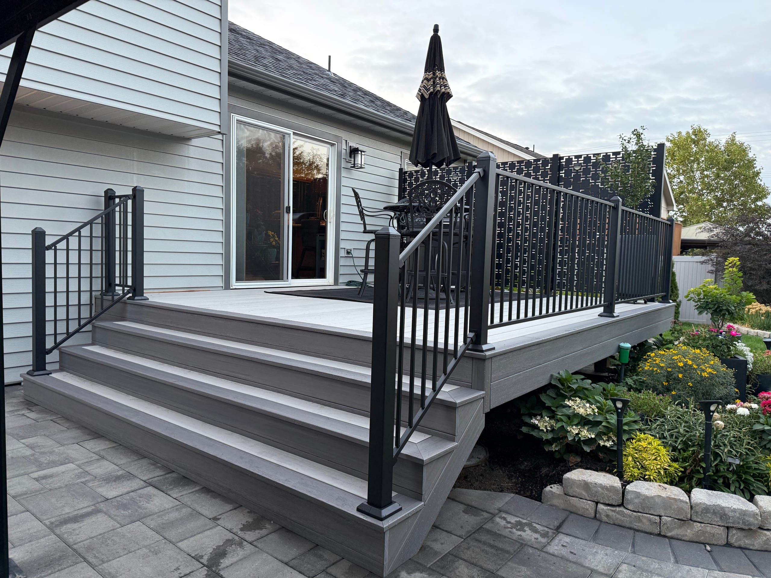 Gray composite deck with wide steps, black metal railing with decorative privacy panel and umbrella