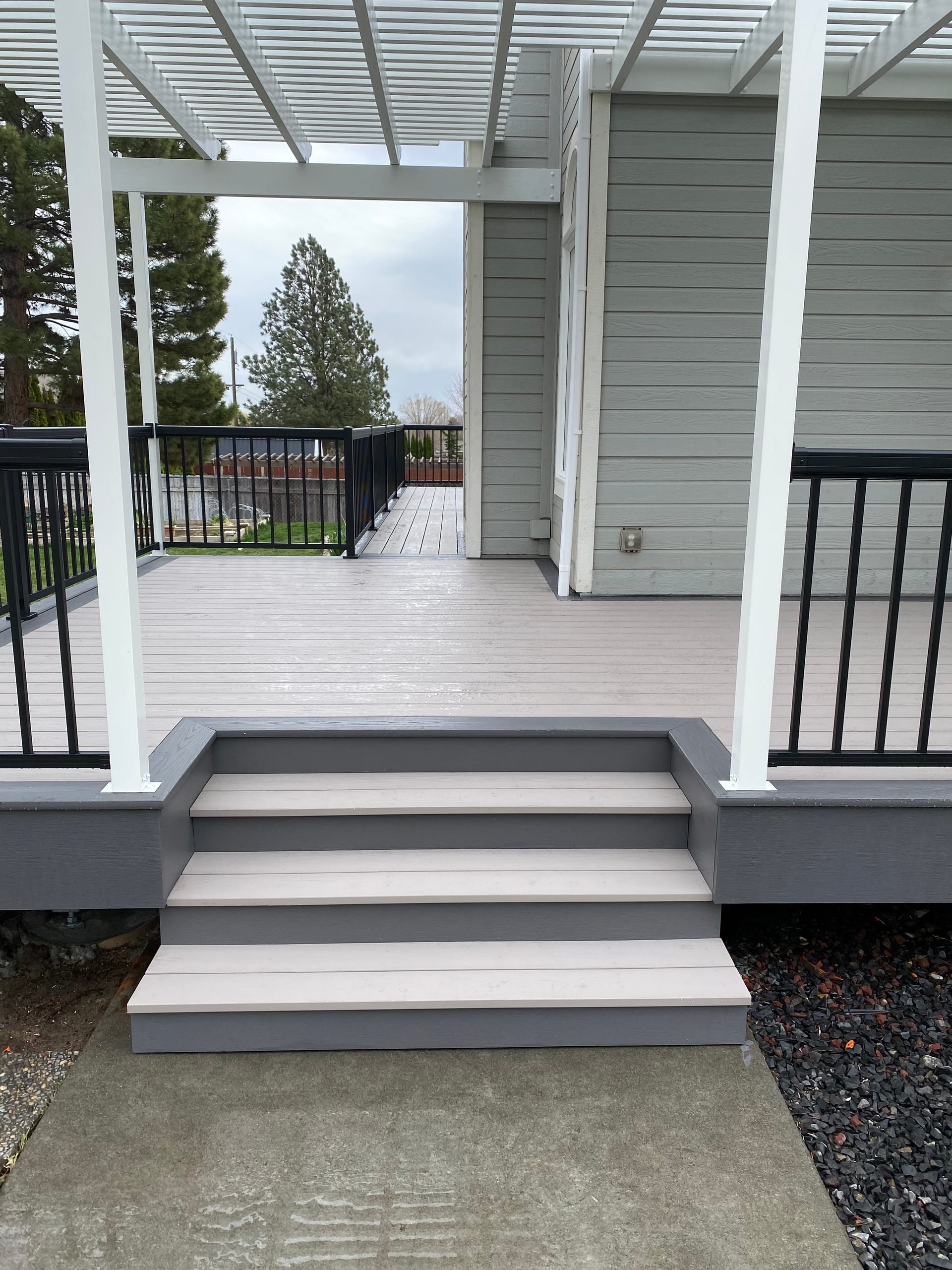 Gray composite porch deck with white posts and white aluminum pergola cover, black railing, gray steps