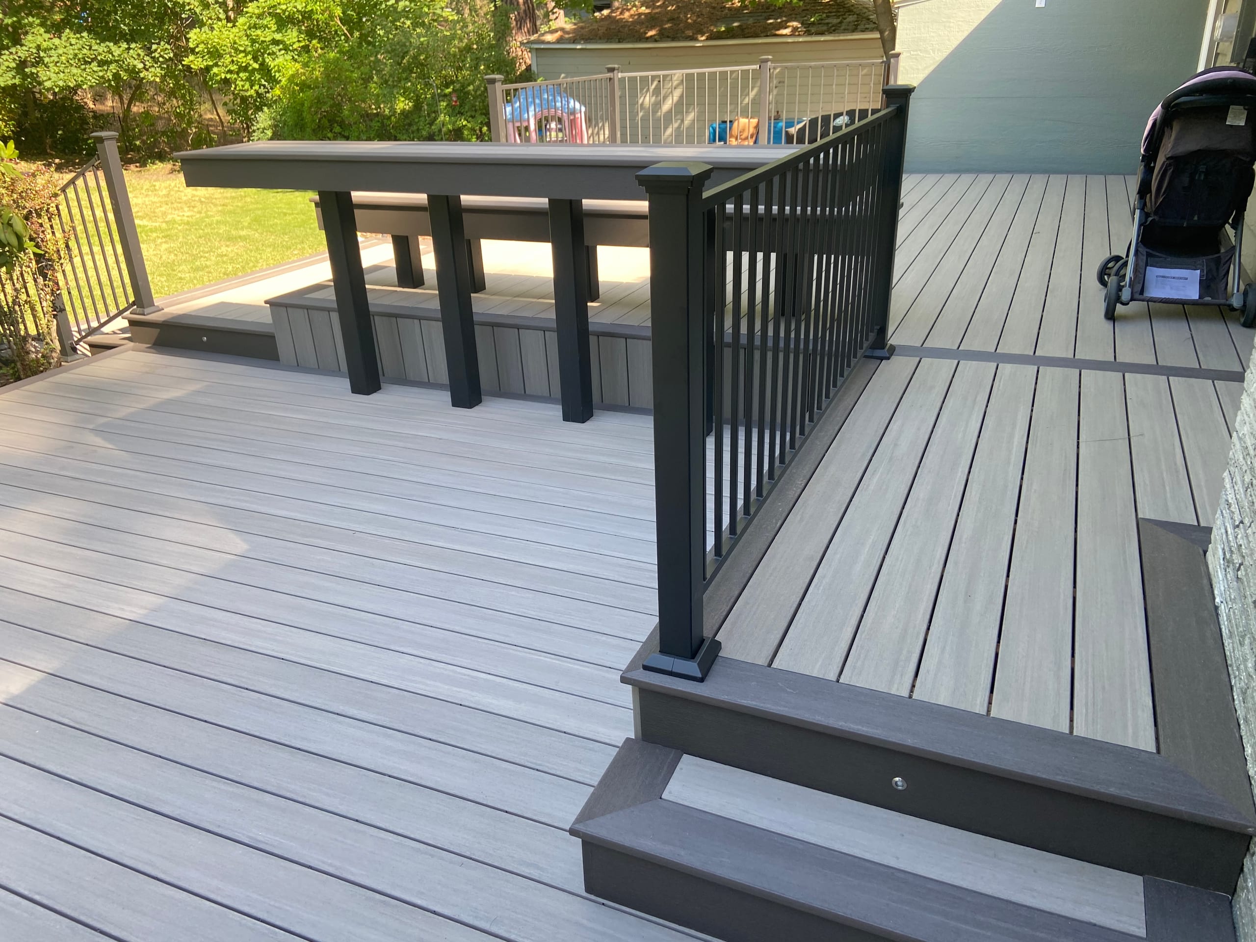 Grey composite deck with bar-height rail ledge on posts and black railing, steps with lighting