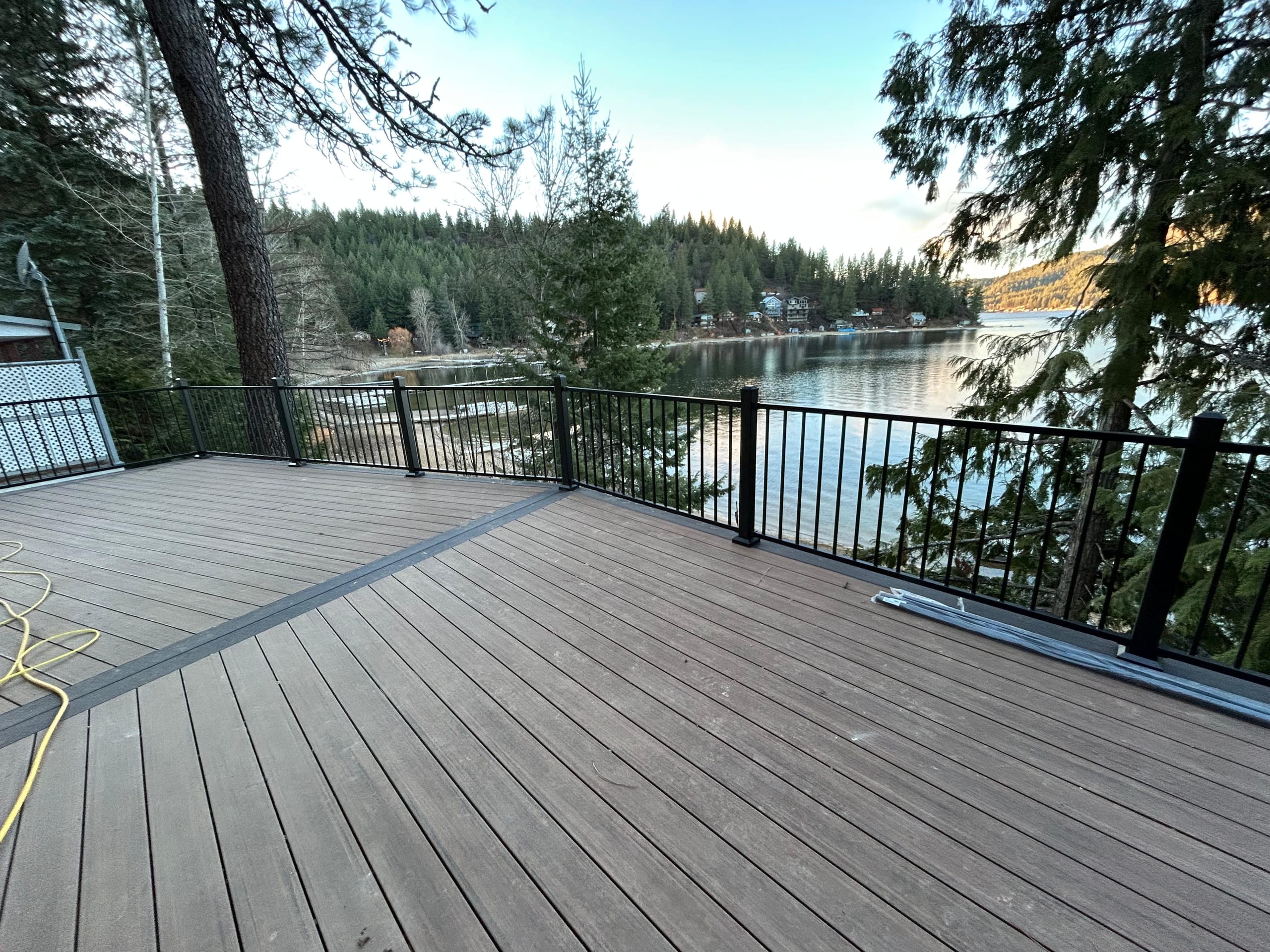 Grey composite deck with dark border and black metal railing overlooking a lake and forested hills