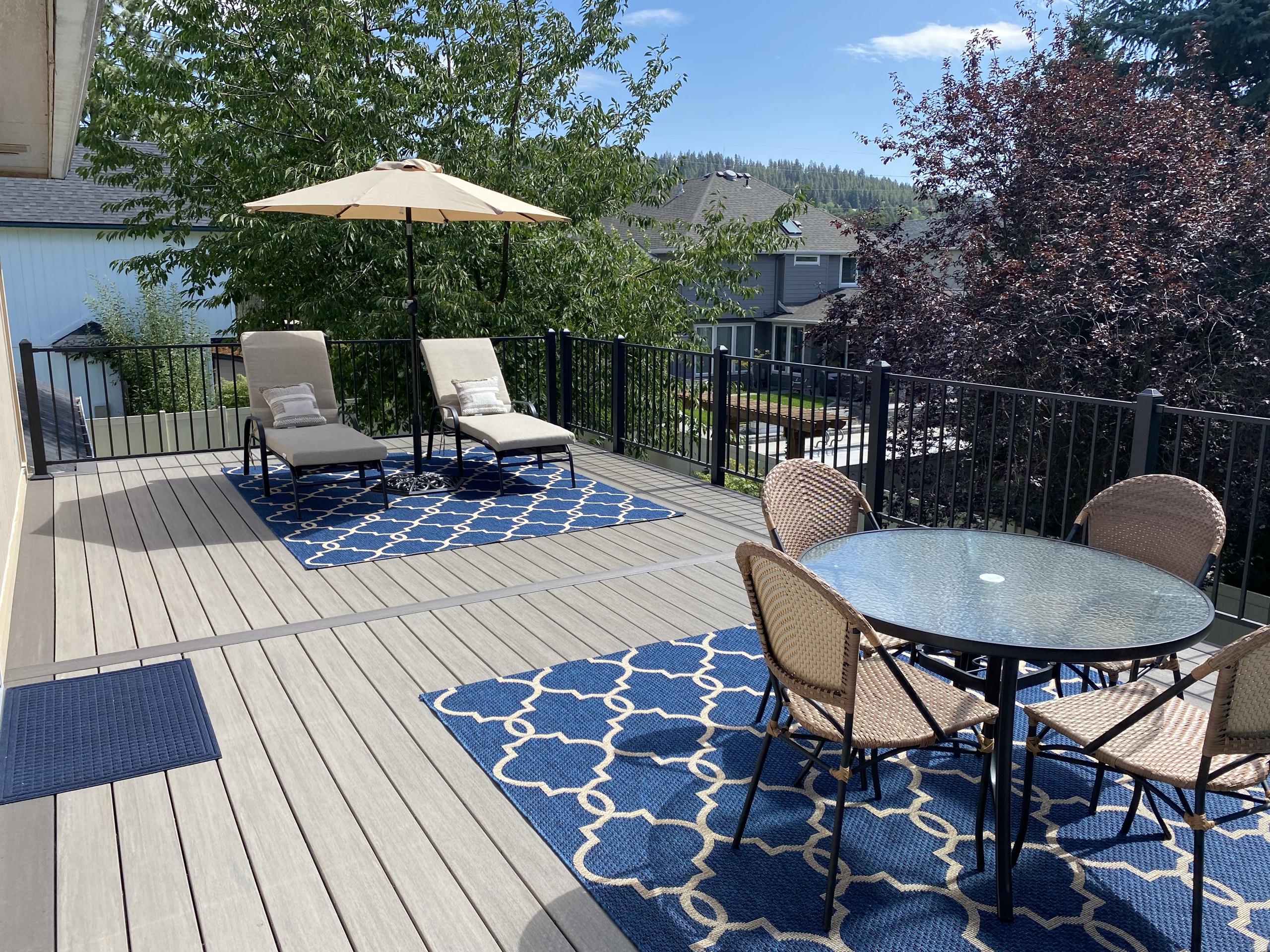 Grey composite deck styled with umbrella, loungers, dining set and blue rugs