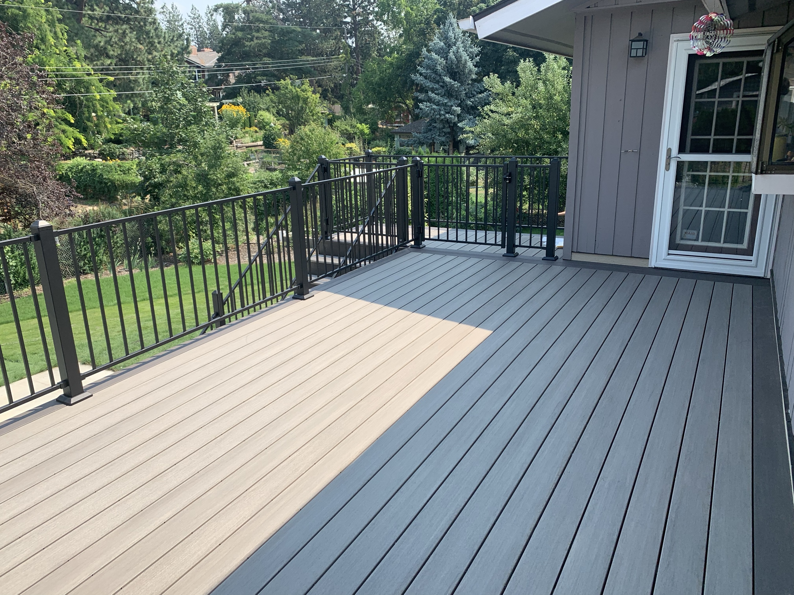 Grey composite deck surface with black metal railing against a house, green yard below