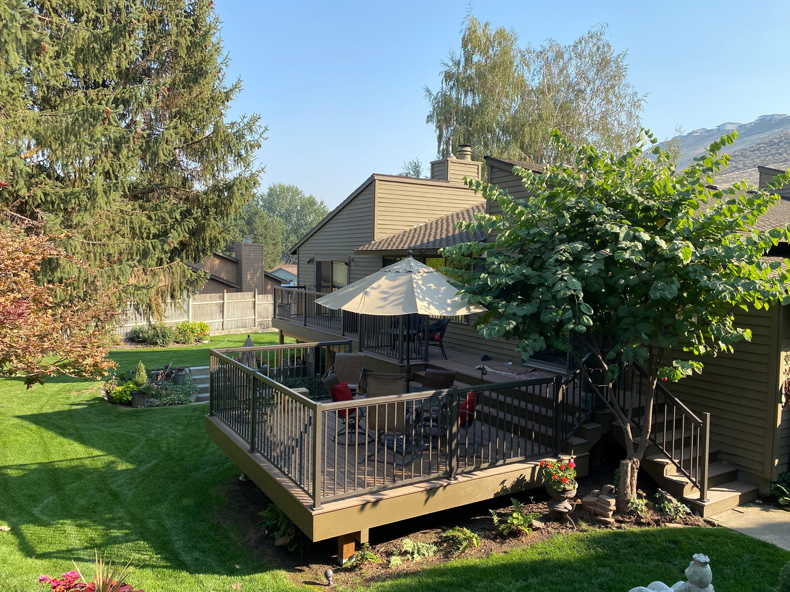 Ground-level gray composite deck with black metal railing, patio table with umbrella and stairs