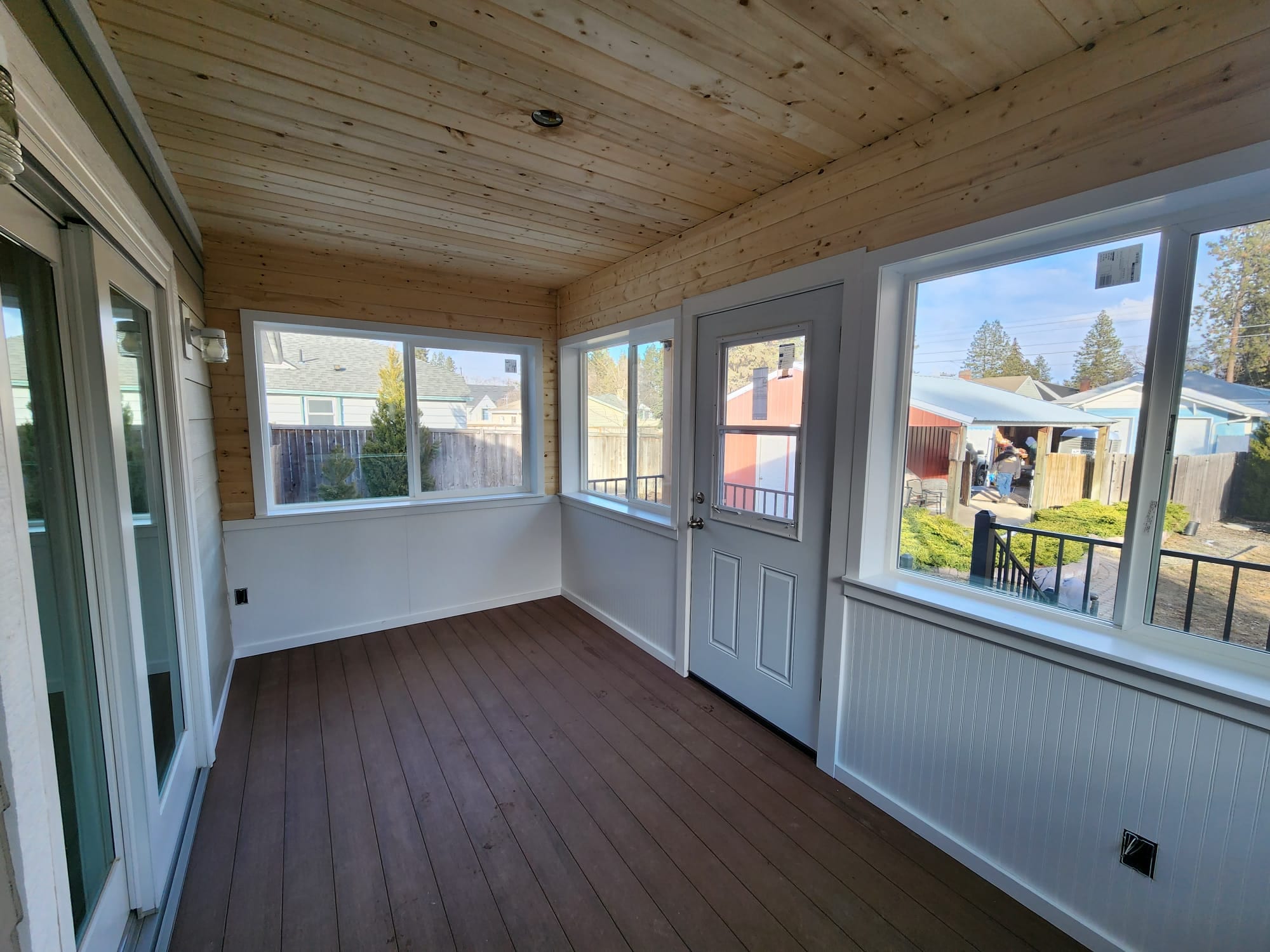 Interior of the enclosed porch with wood-plank ceiling, windows with neighborhood view, white door and composite floor