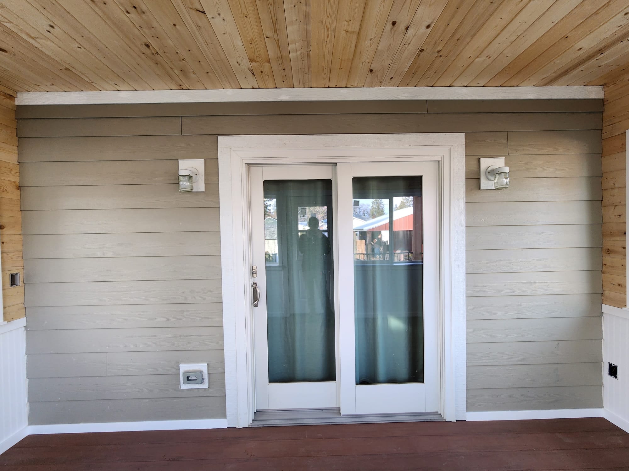 Interior wall of the enclosed room with sliding patio door, siding walls, wood ceiling and dark composite floor