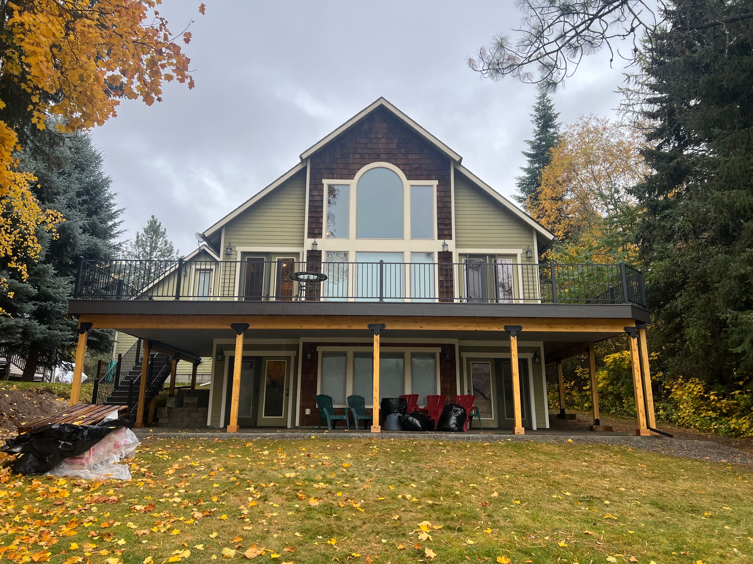 Lakeside A-frame style chalet with elevated gray deck and black railing above a covered lower level, autumn lawn and trees