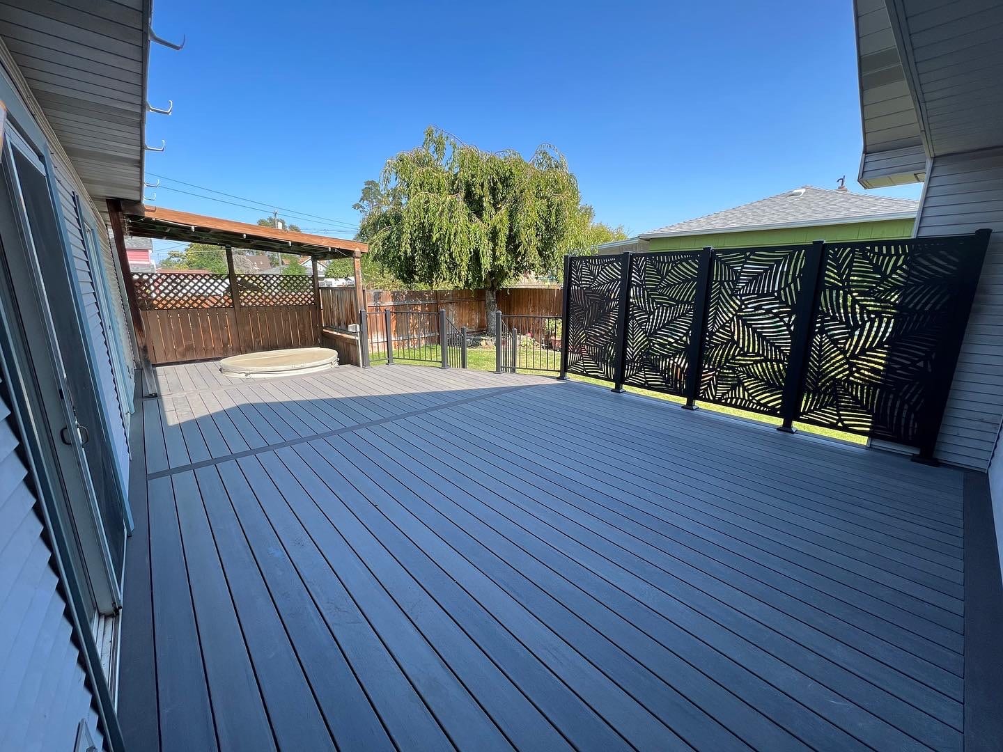 Large dark gray composite deck with black leaf-pattern privacy screen along far railing, sunny sky