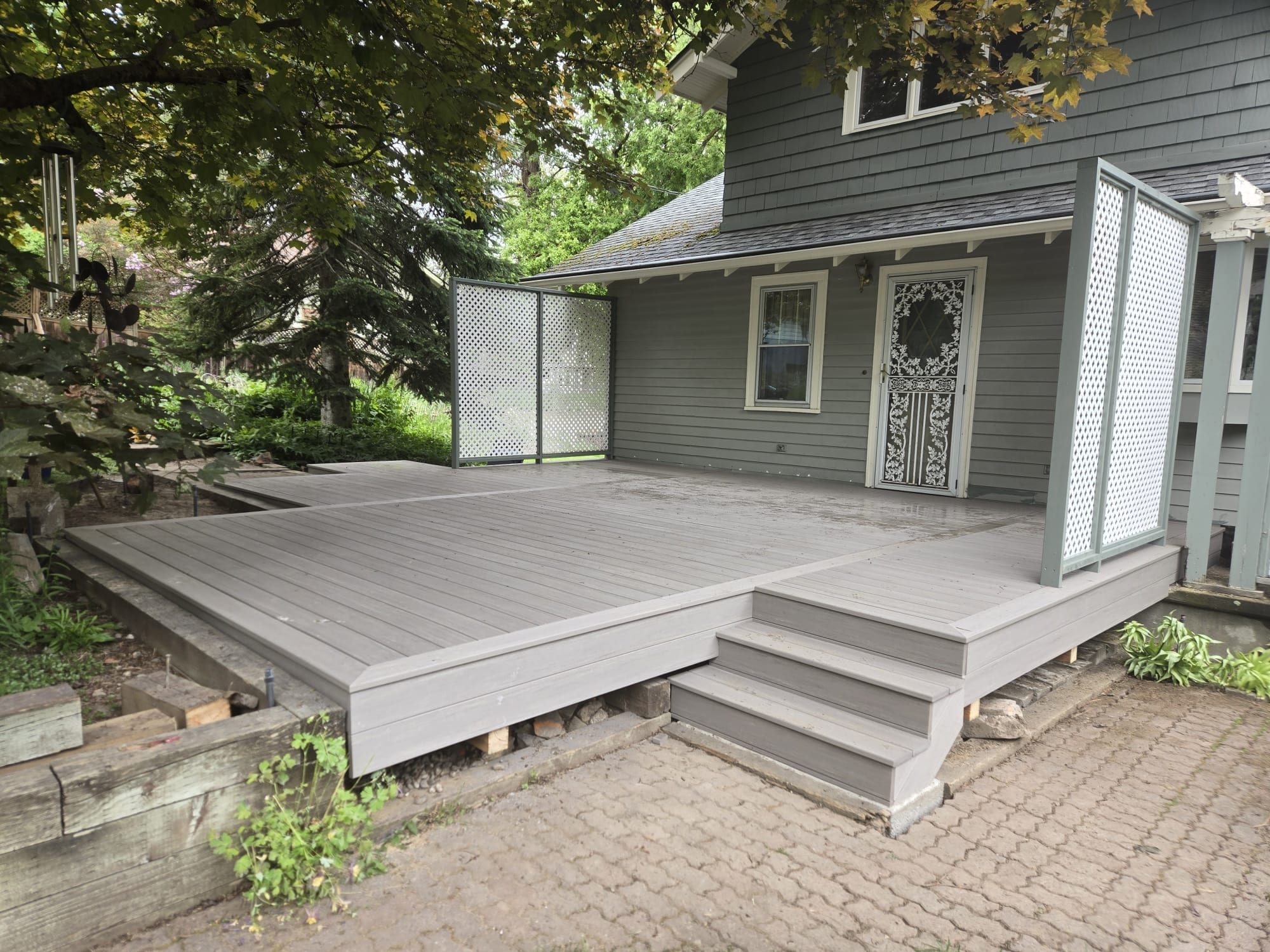 Large light grey composite deck platform with wide steps and a privacy screen panel on a paver patio at a grey house