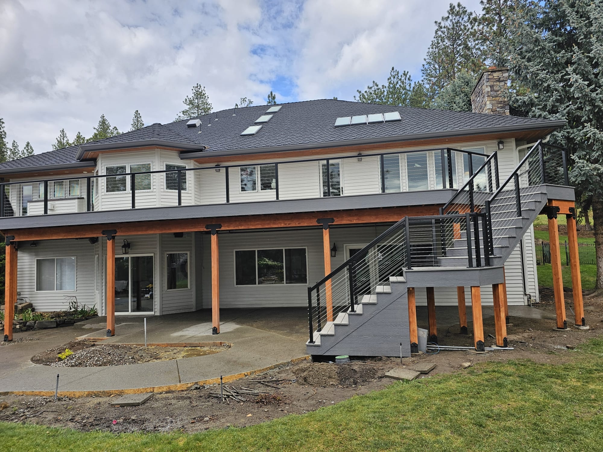 Large two-story home with elevated deck with cable railing, cedar posts, gray stairs and covered patio below