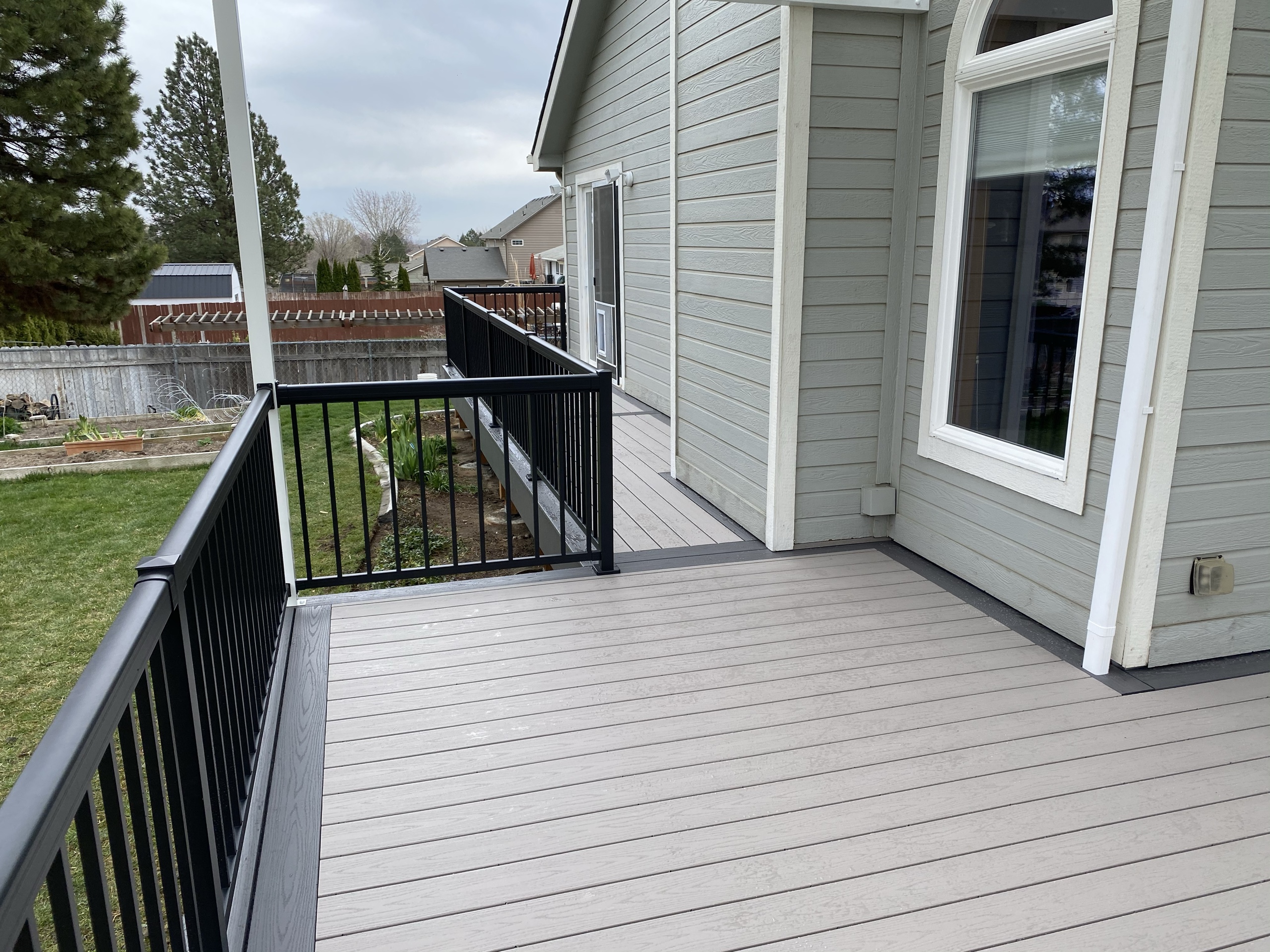 Light gray composite deck with black picket railing beside gray house with white trim and window