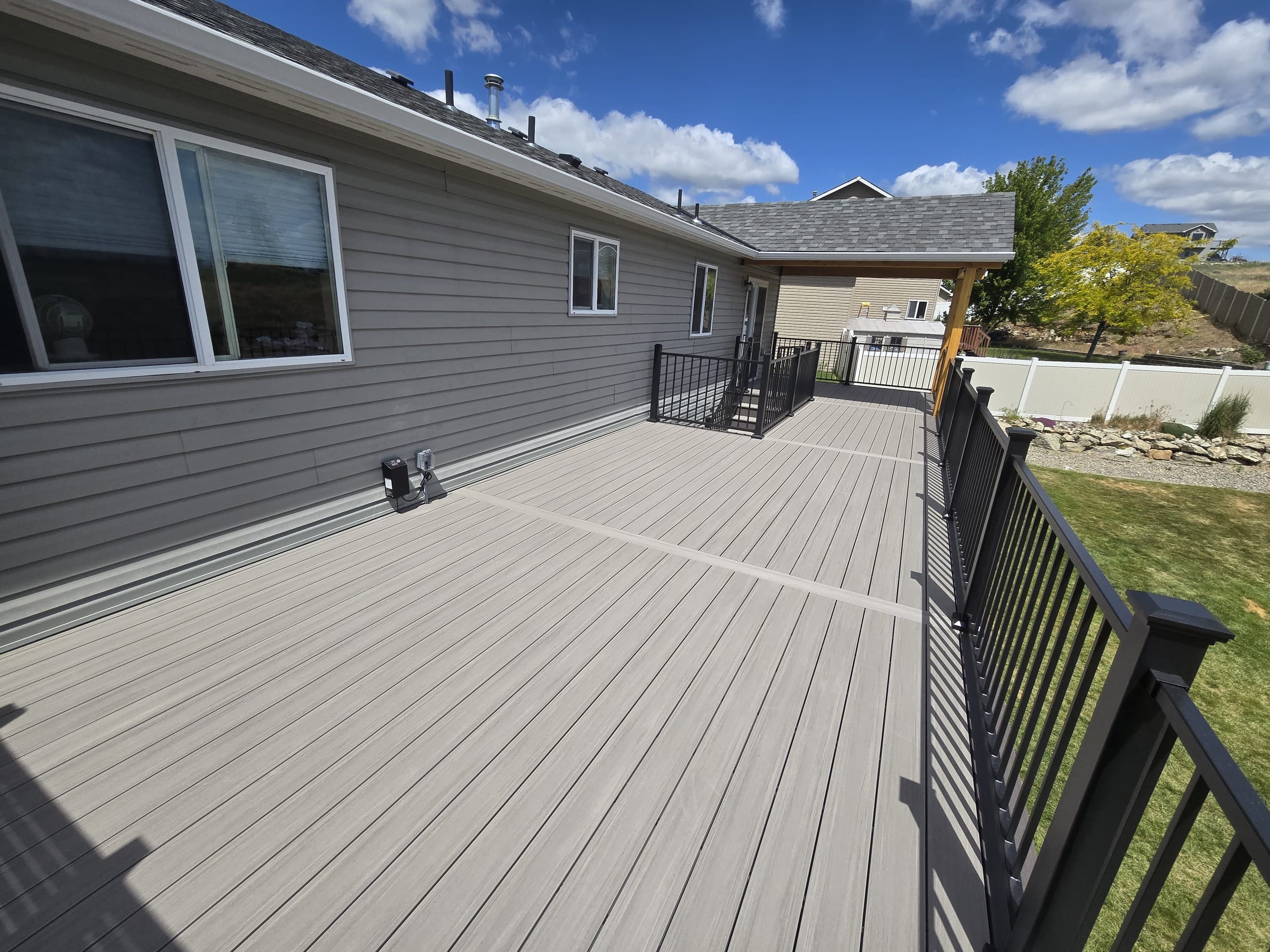 Long grey composite deck along a grey house with black metal picket railing and blue sky