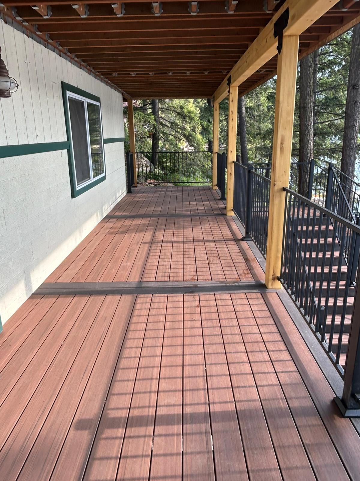 Long reddish-brown composite deck walkway beneath a wood-ceilinged roof with black metal railing, along beige house