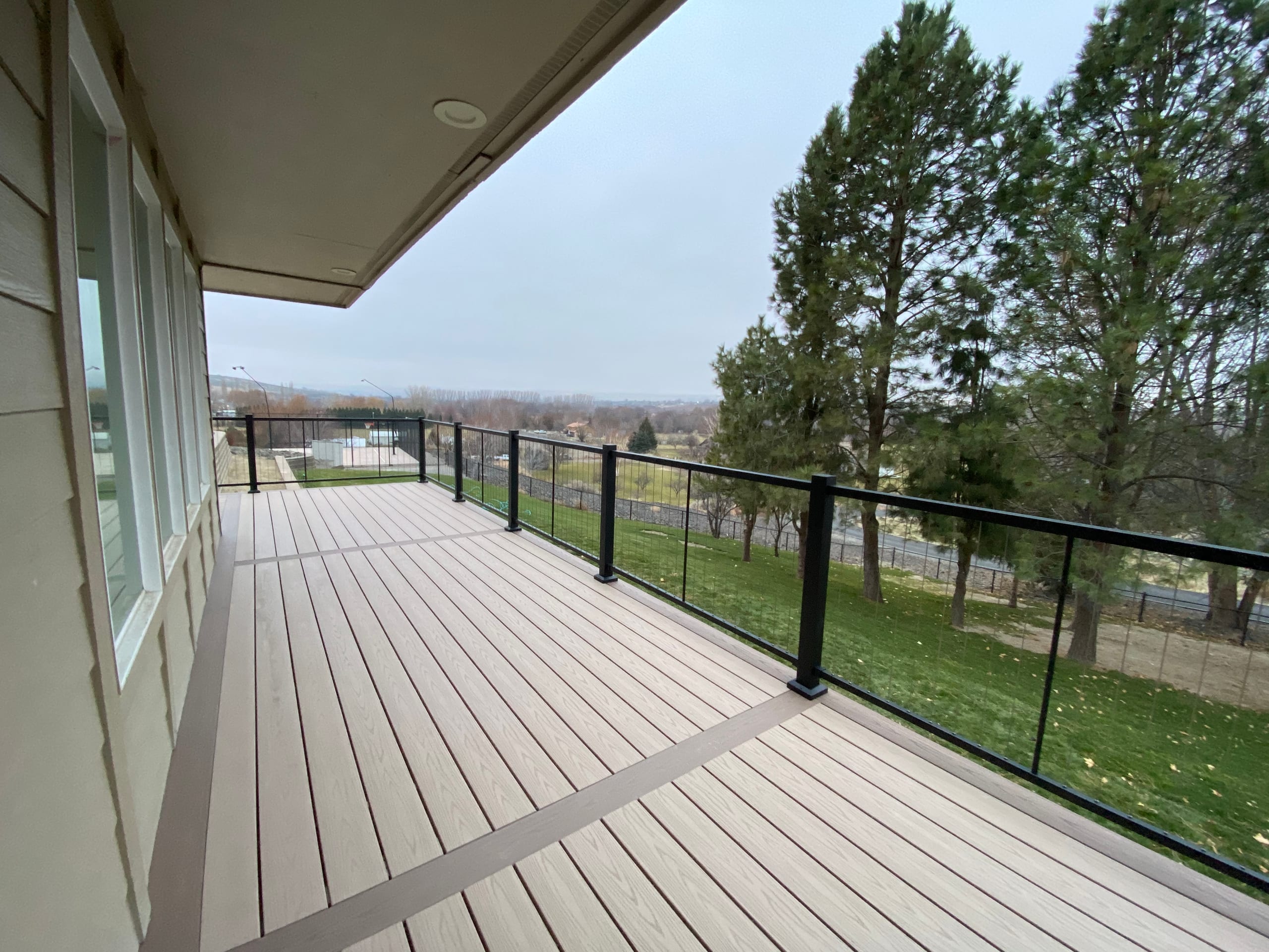 Long tan composite deck with diagonal accent border and black cable railing, pines and valley beyond