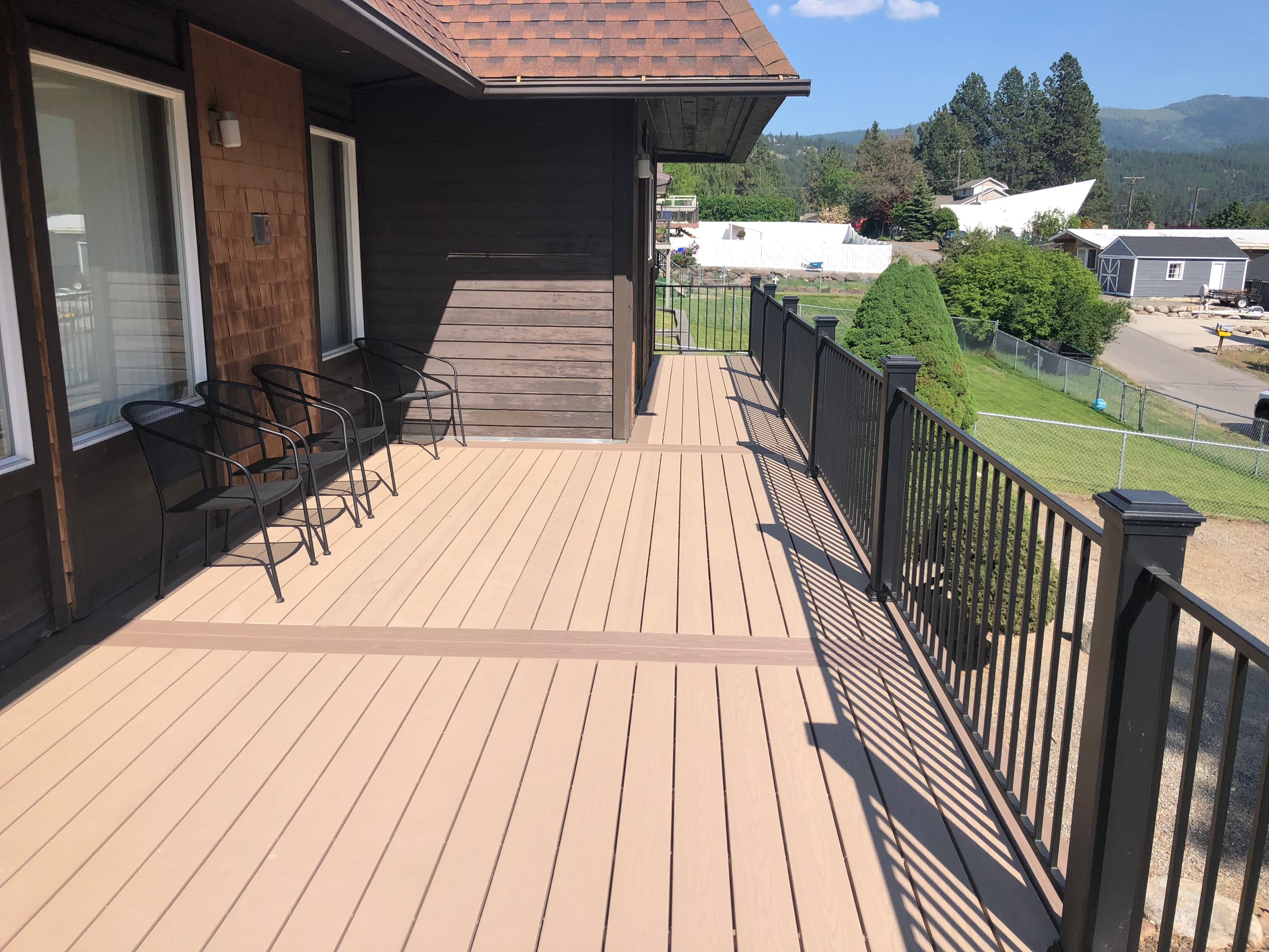 Long tan deck with black metal railing along the side of a dark-sided house