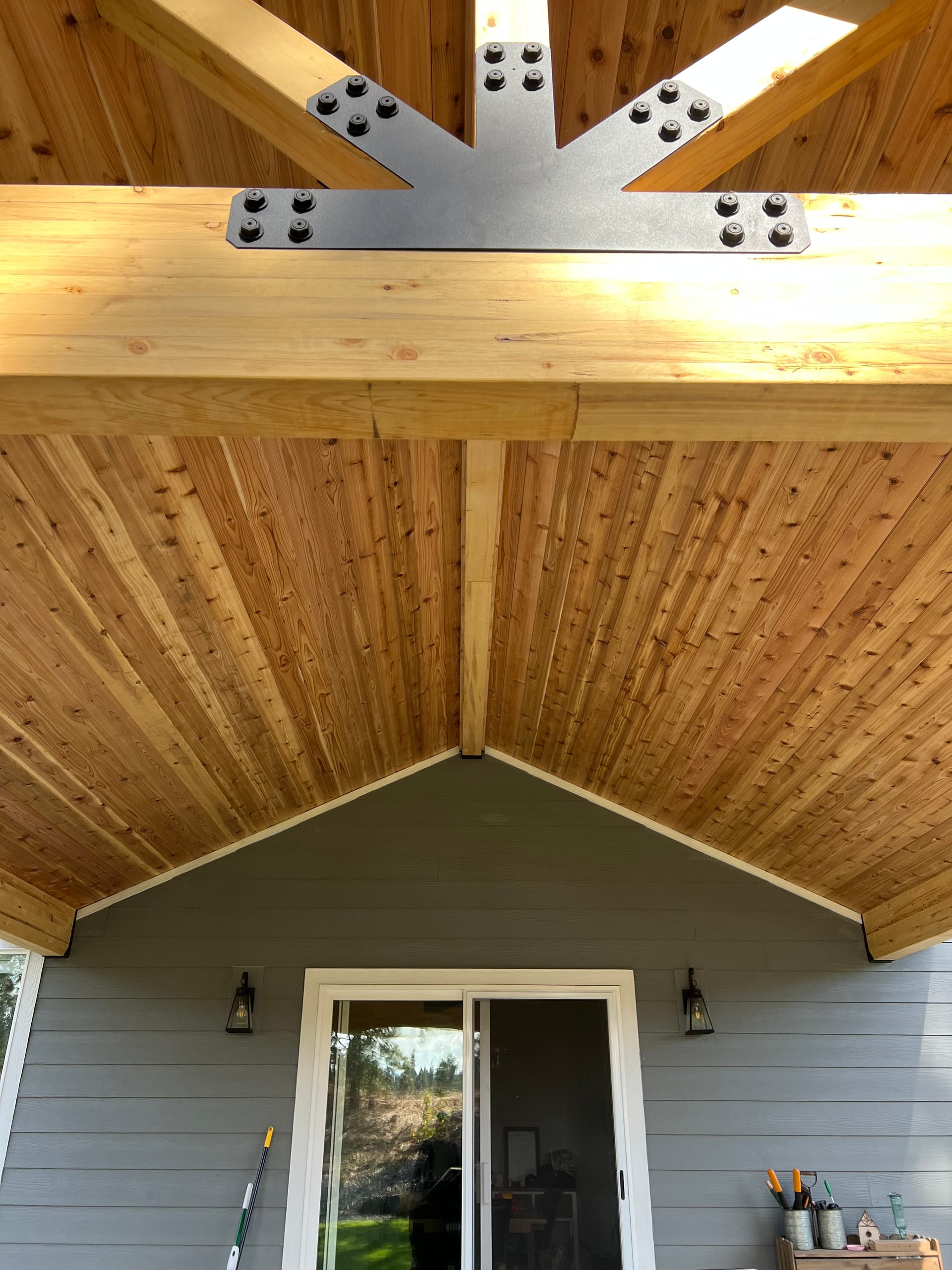 Looking up at cedar vaulted ceiling with black steel truss gusset plates, above a sliding door on gray siding
