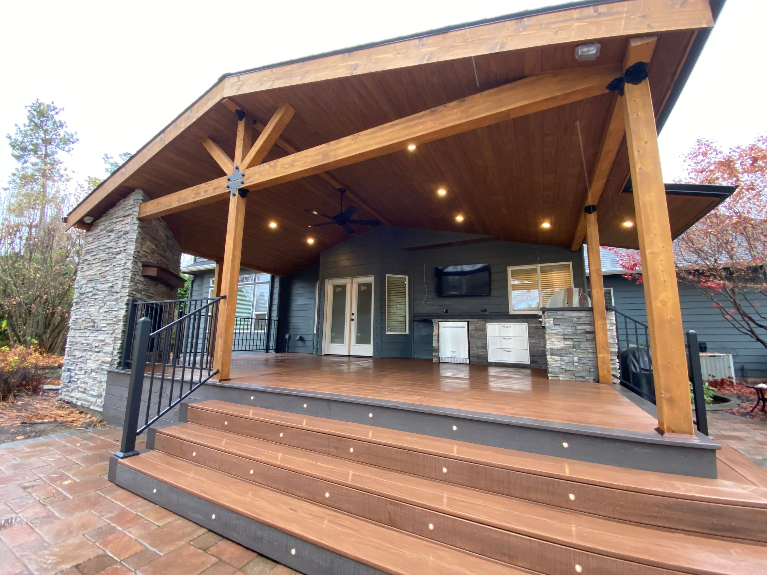 Low-angle view up wide stepped landing with step lights into a gabled covered deck with timber trusses