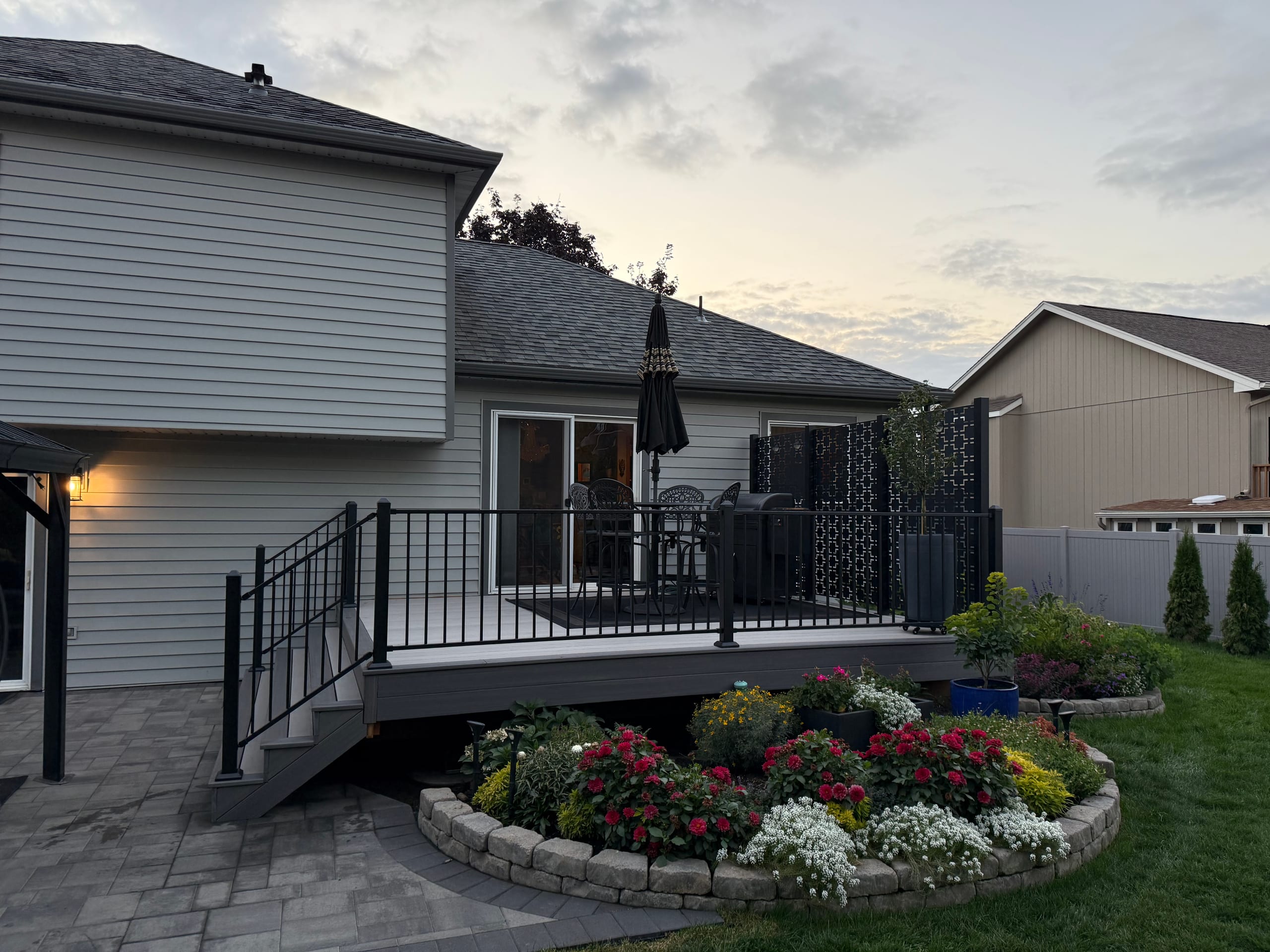 Low gray deck with black metal railing and privacy screen panels above a paver patio