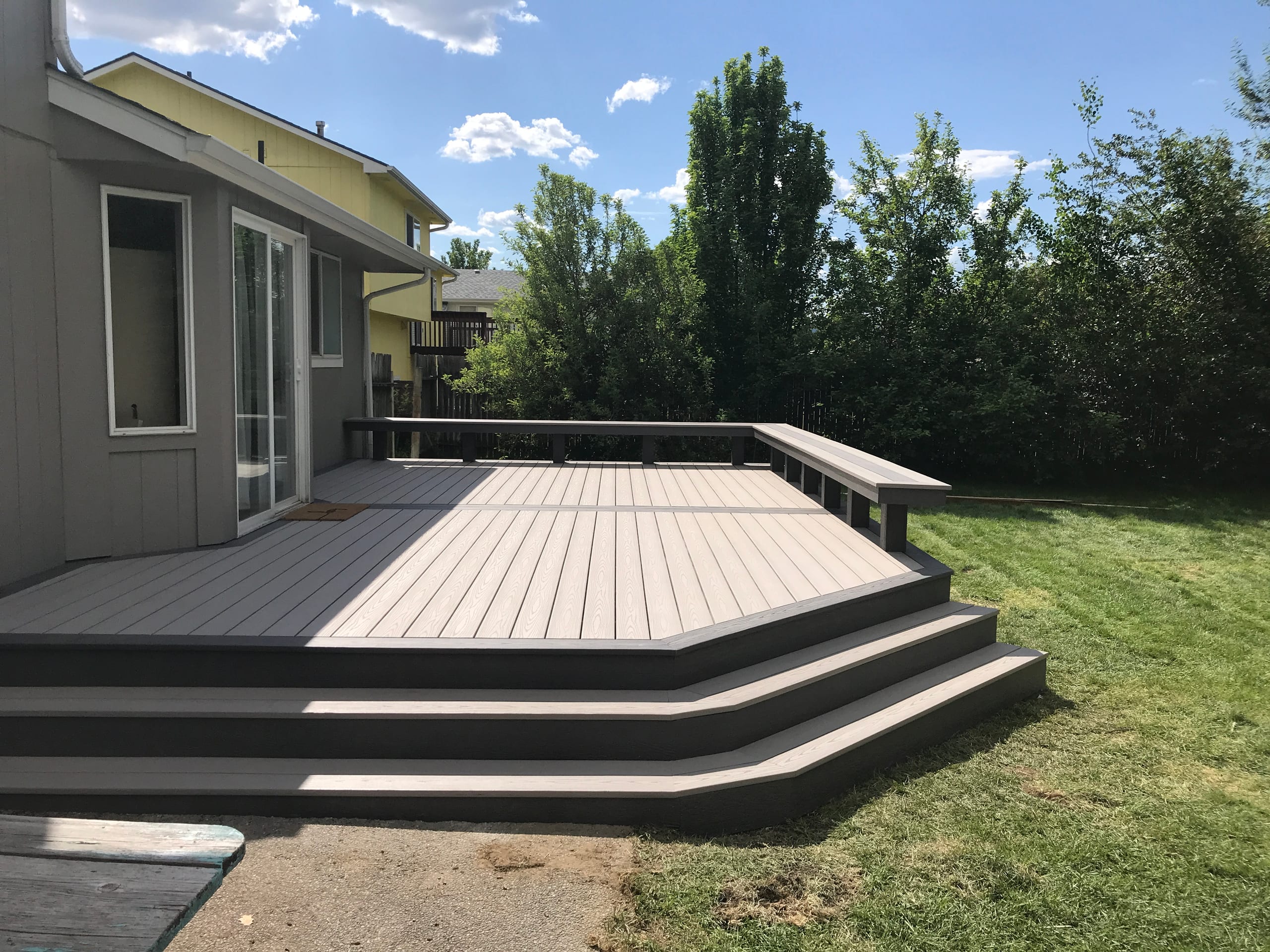 Low gray deck with wraparound steps and a built-in bench along the edge