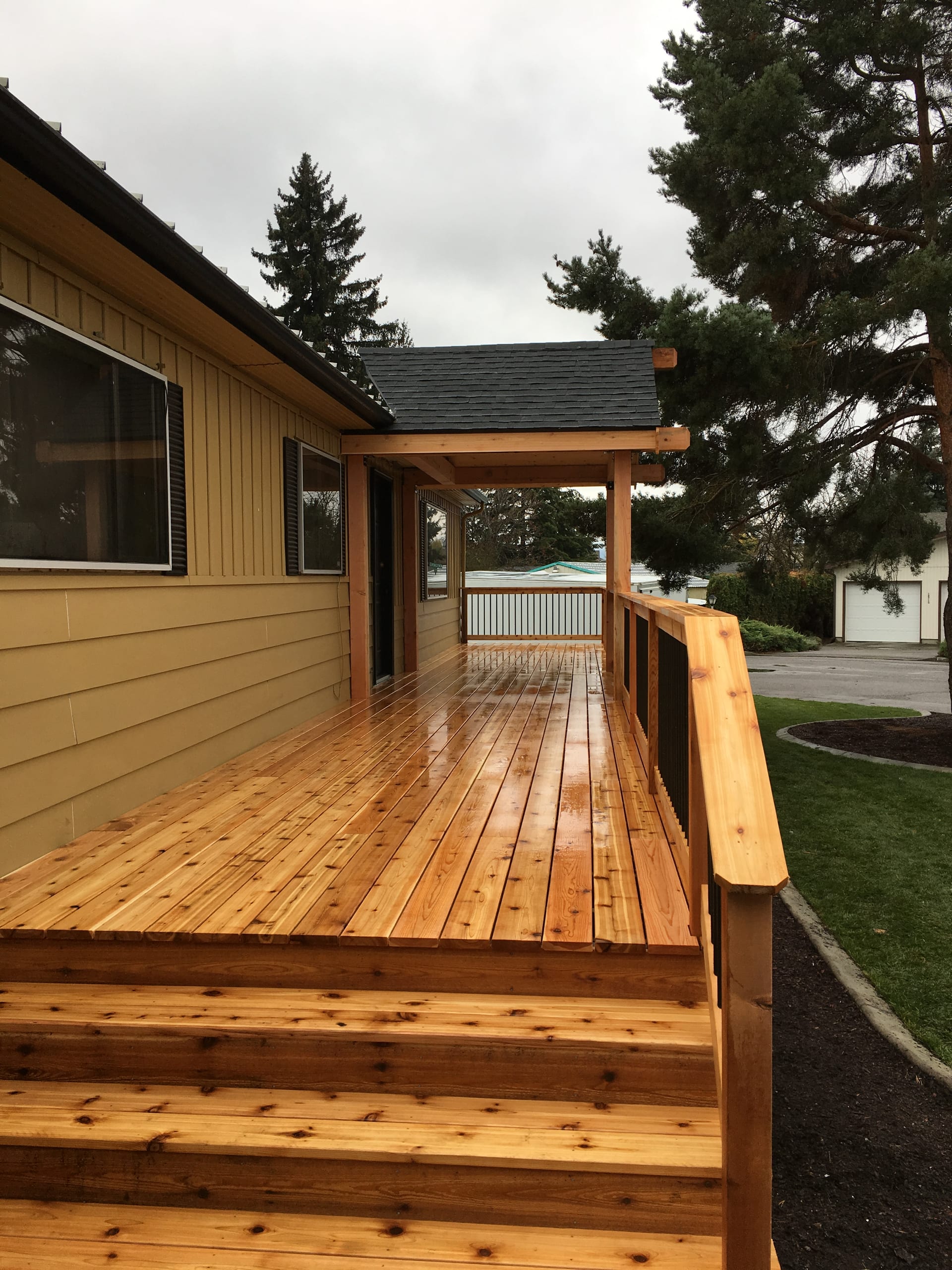 New cedar deck and wide cedar steps with wood railing beside a yellow house, wet boards