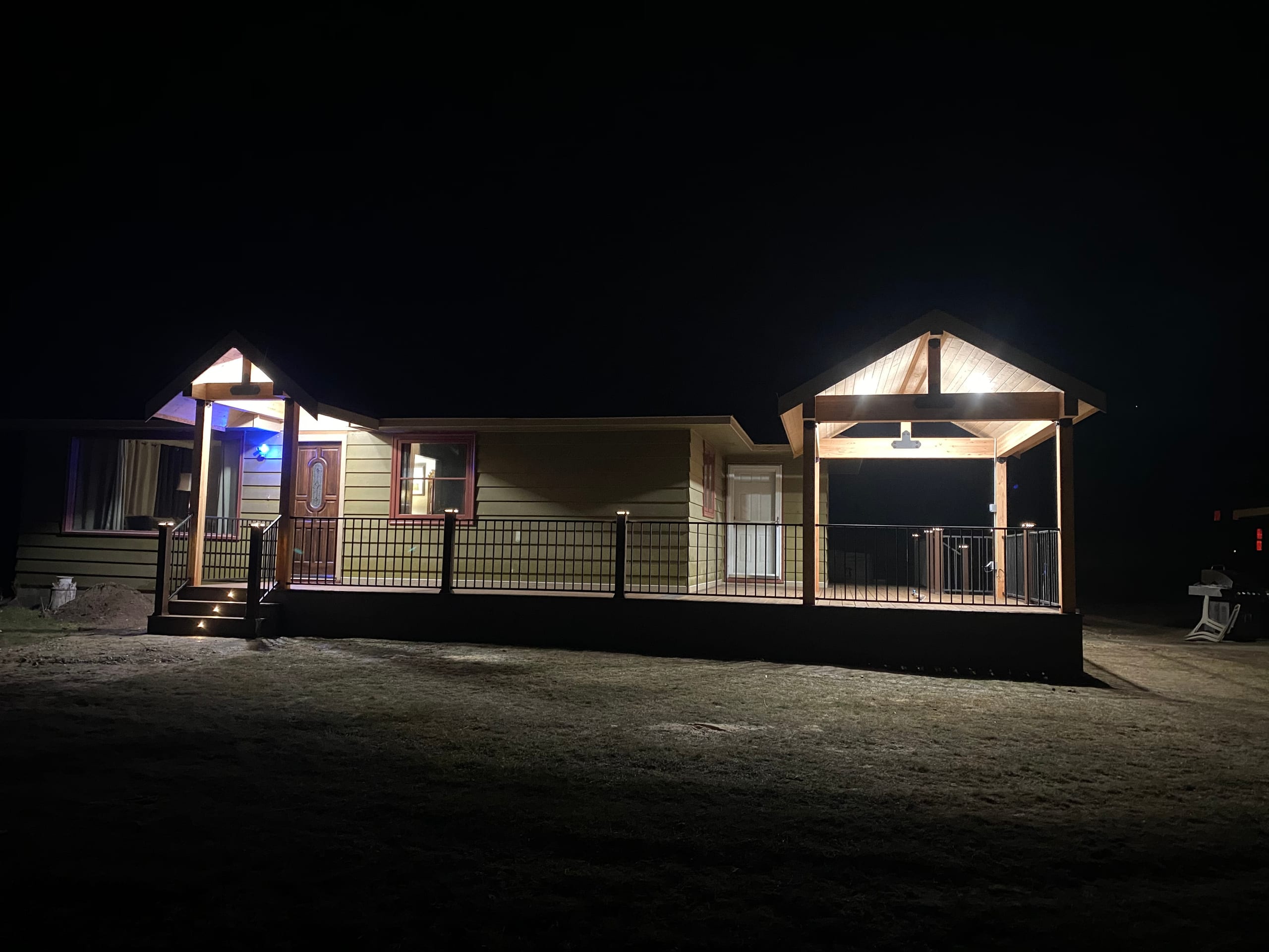 Night view of house with two lit gabled covered decks and steps, dark yard