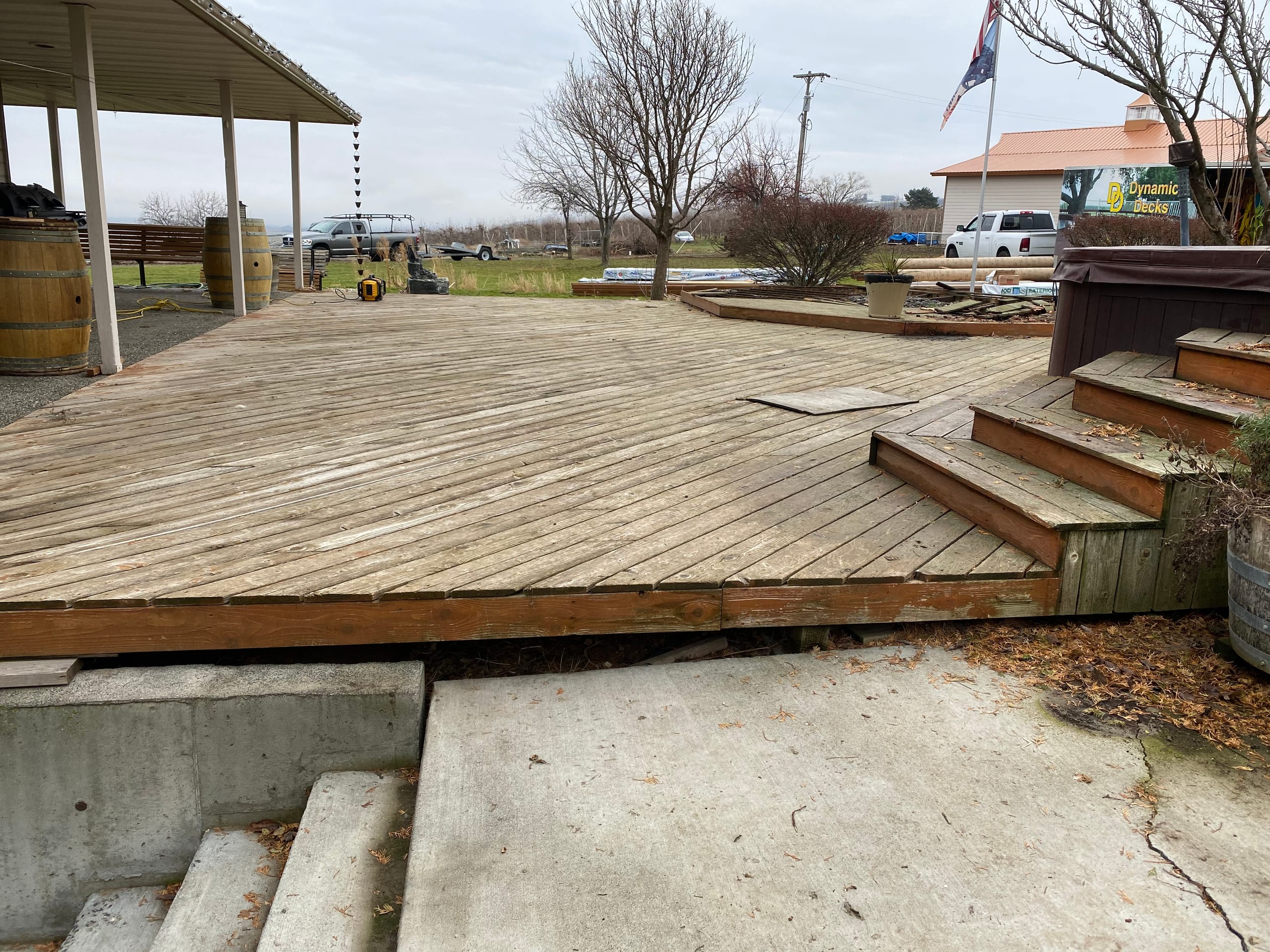 Old weathered grey wood deck with wide steps down to cracked concrete, hot tub and flag in background, rural field