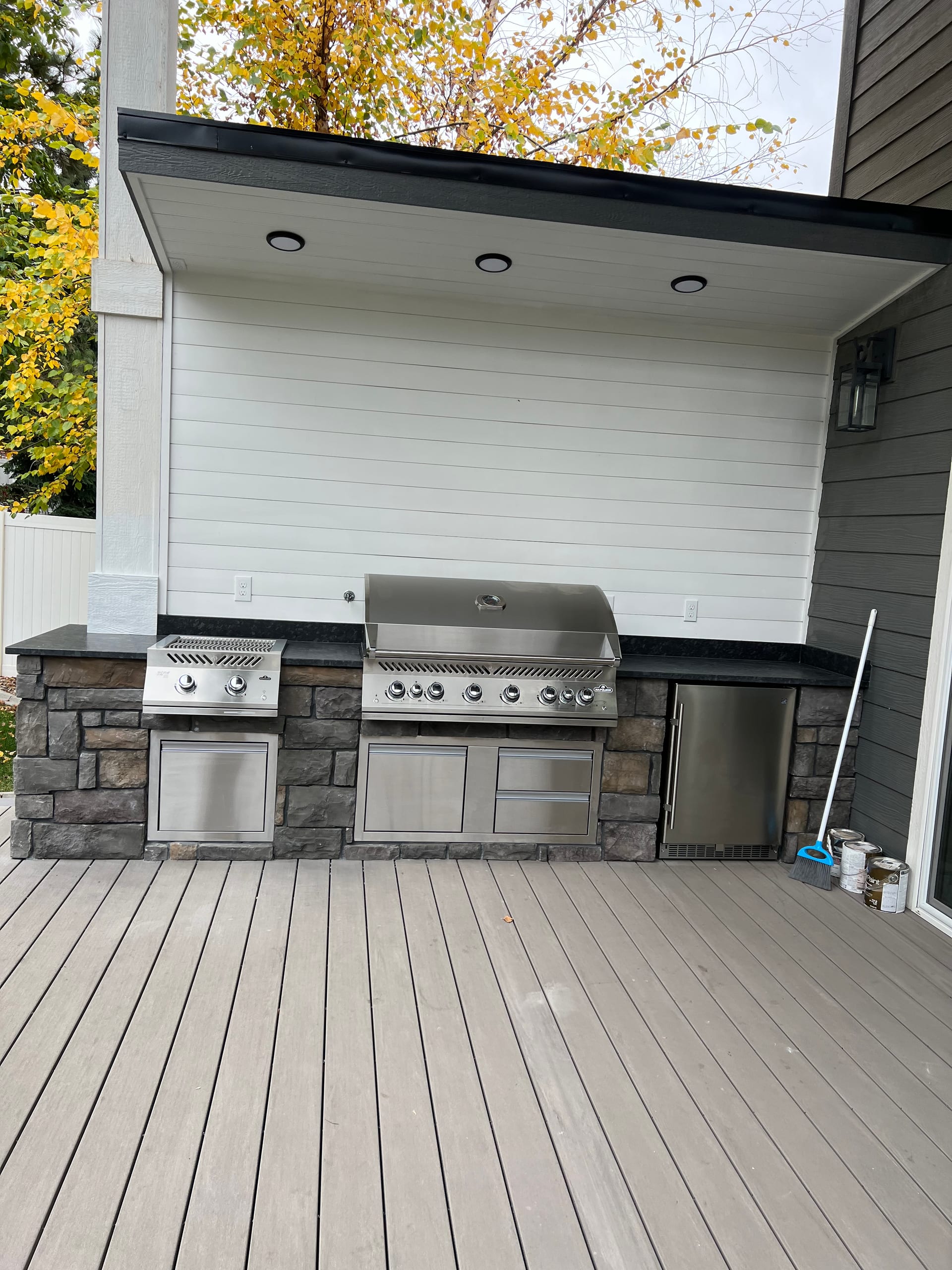 Outdoor kitchen with stainless grill on stone base under white canopy, gray composite deck foreground