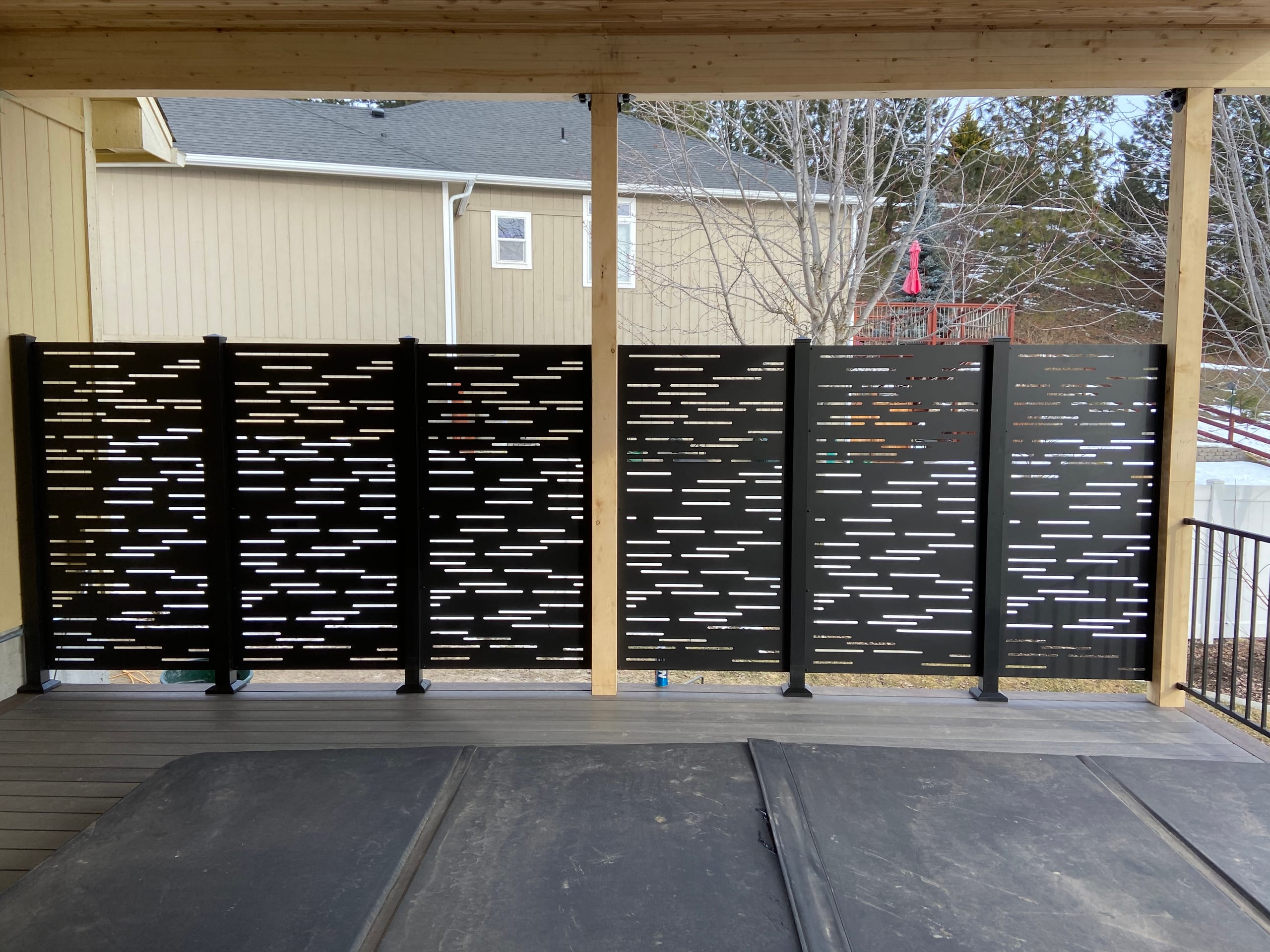 Perforated black metal privacy screen between wood posts under cedar covered deck roof, grey decking