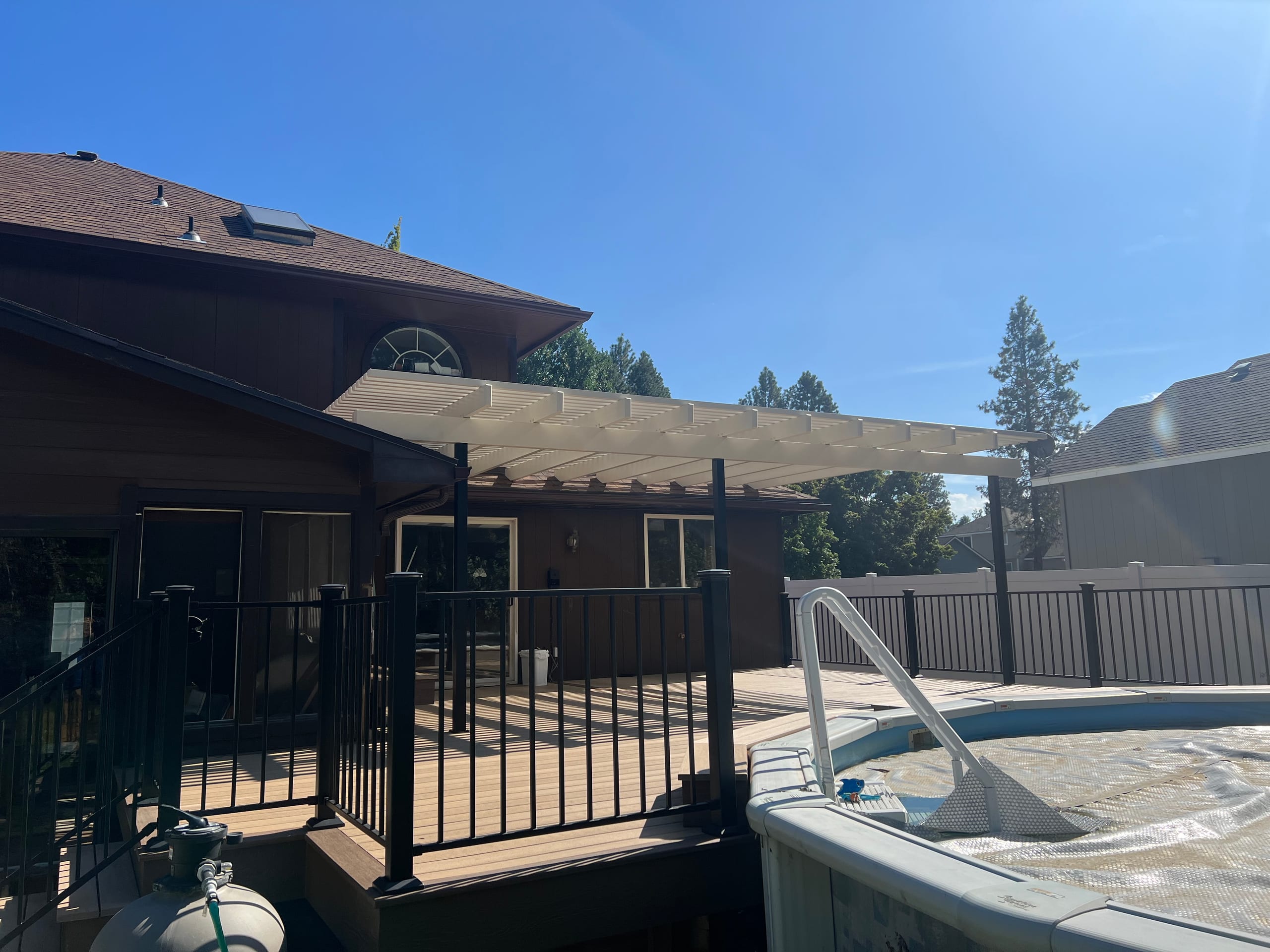 Pool deck with black metal railing, composite boards and white pergola cover against dark brown house